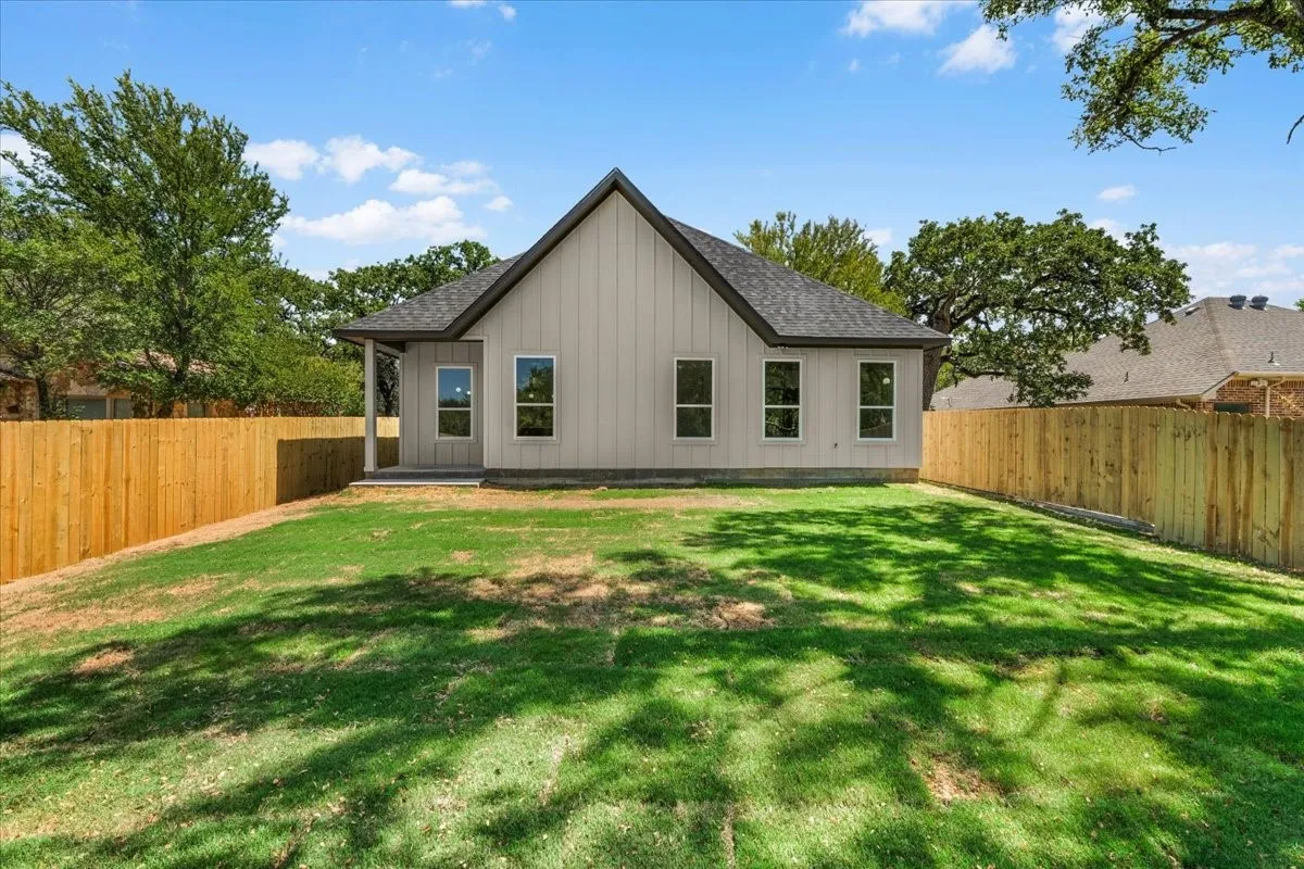 Expansive grassy yard with a newly installed wood fence, featuring a back patio and multiple windows