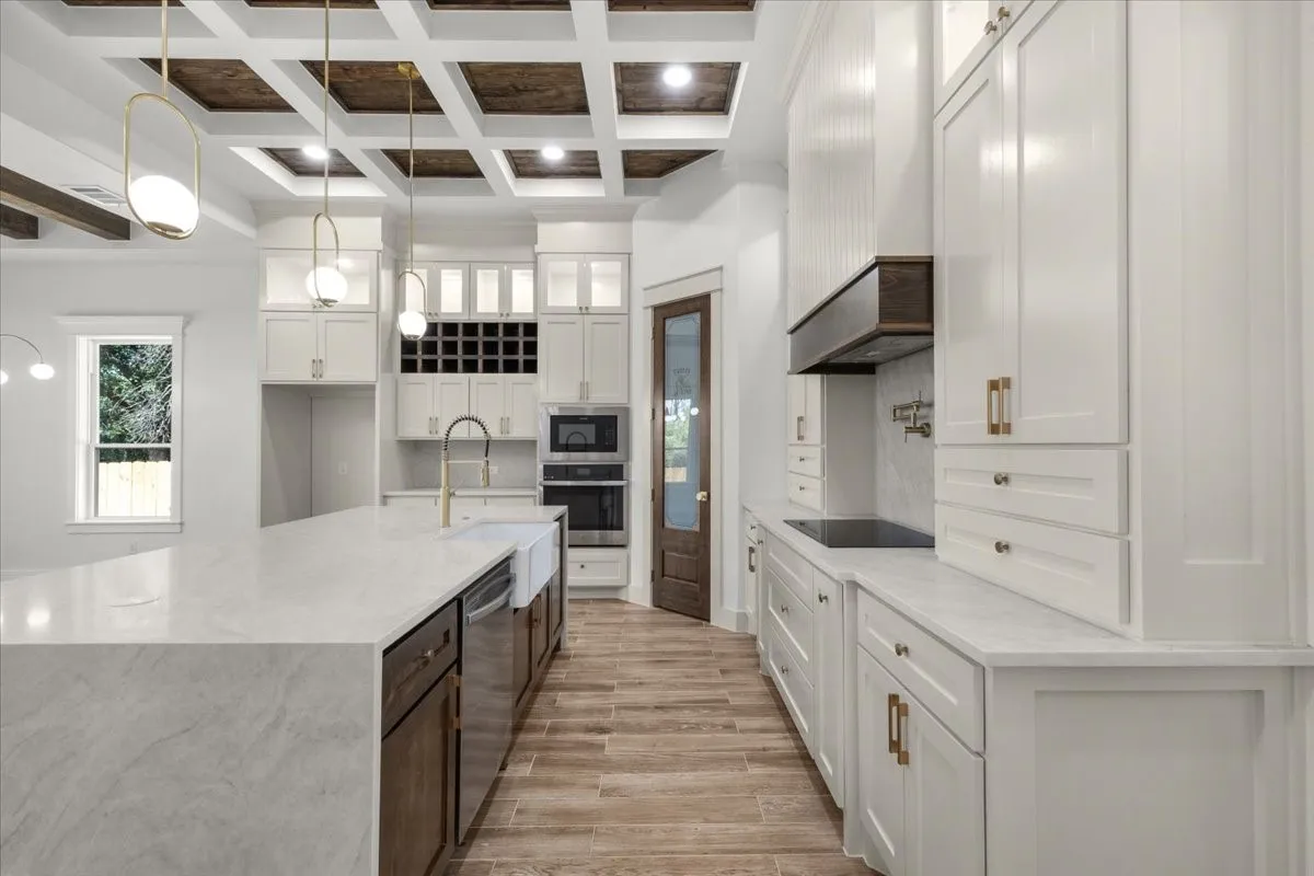 Coffered ceiling with wood paneling, white shaker-style cabinetry, large kitchen island with light-toned countertop, integrated oven, and wood-finish flooring