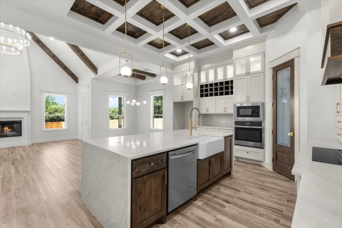 Kitchen featuring a coffered wood-panel ceiling, central island with an integrated sink, built-in stainless steel appliances, and wood-finish flooring
