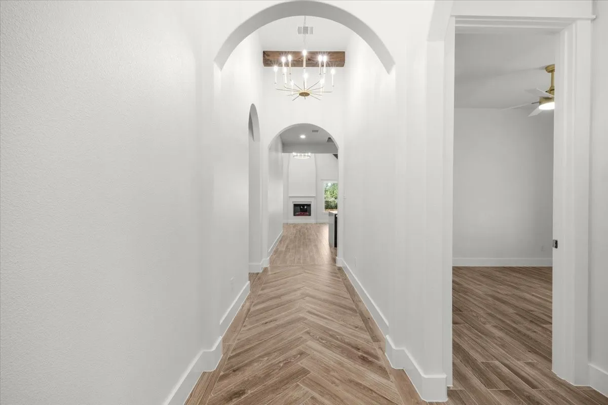 Arched doorways, wood-finish flooring in a herringbone pattern, contemporary chandelier, and a decorative exposed wood beam