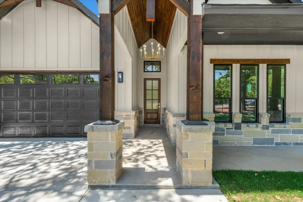 Architectural facade featuring a gabled roofline, board and batten siding, stone veneer accents, wood-clad columns, and a glass-paneled entry door