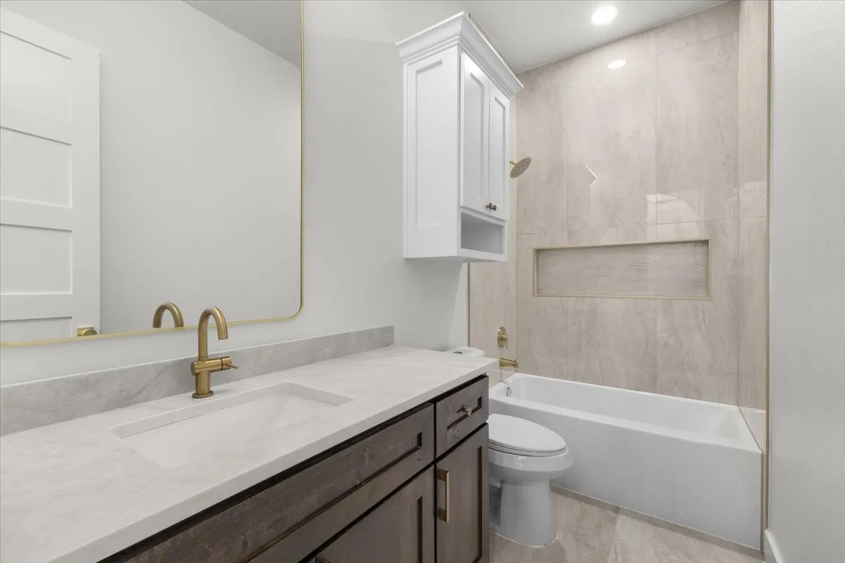 Built-in bathtub with a tiled surround, recessed shower niche, and gold-finish fixtures