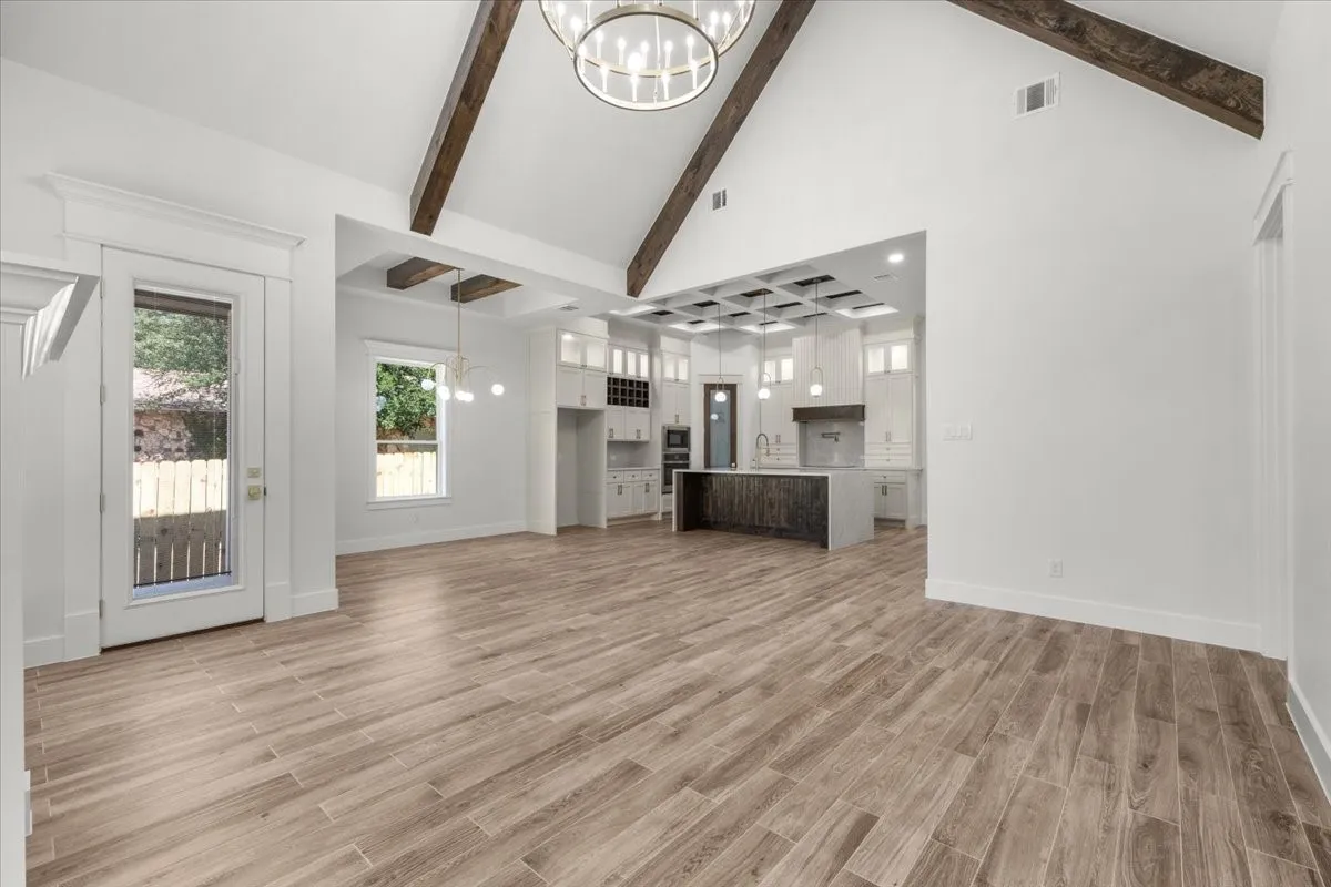 Vaulted ceiling with exposed wood beams, wood-finish flooring throughout, kitchen with coffered ceiling and central island, built-in shelving, and recessed lighting