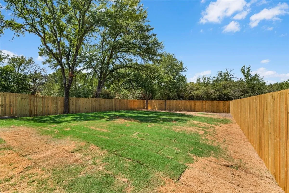 Expansive rear yard with privacy fencing, mature trees, and partial sod installation
