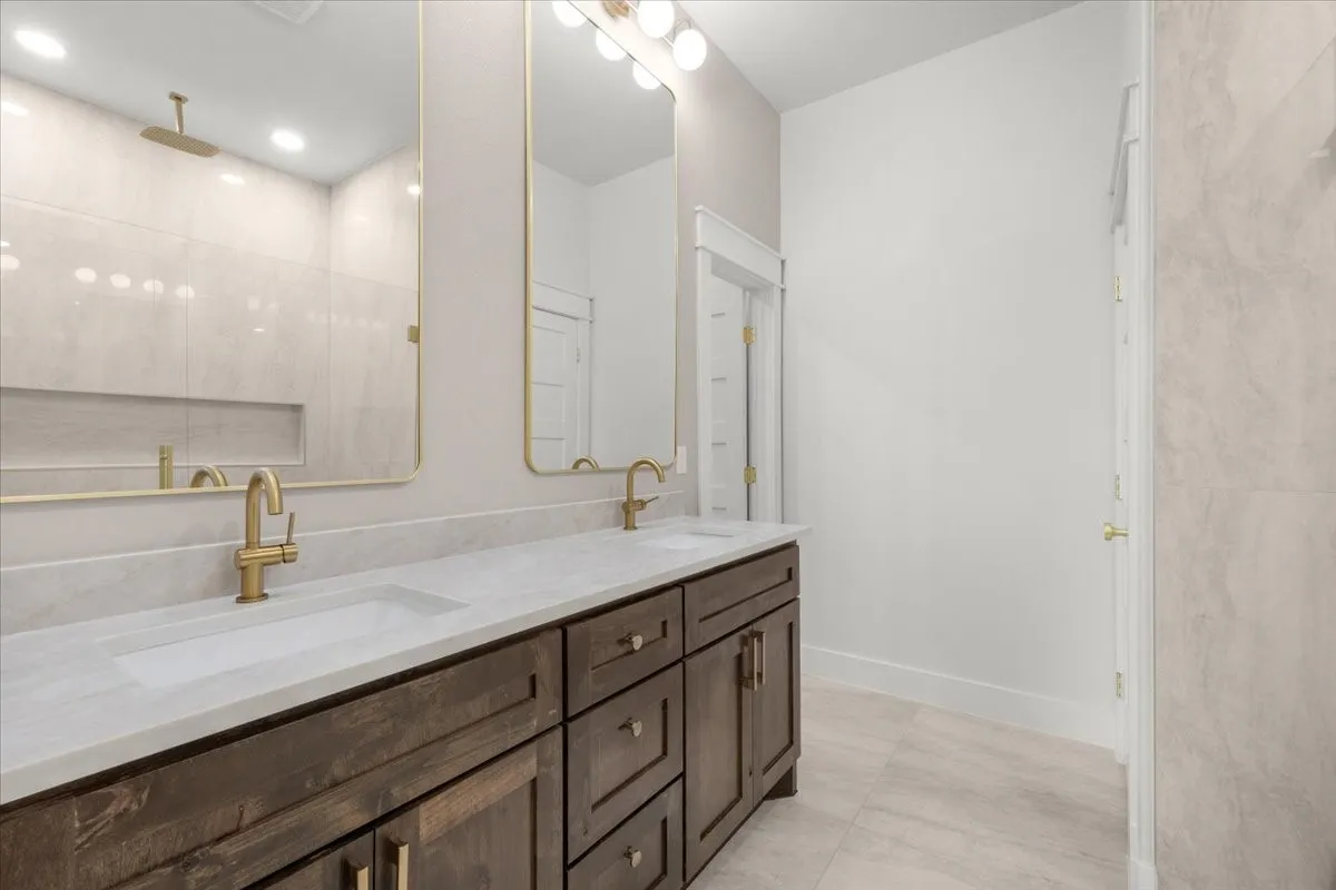 Double vanity with dark wood-finish cabinetry, integrated sinks, and brass-finish faucets