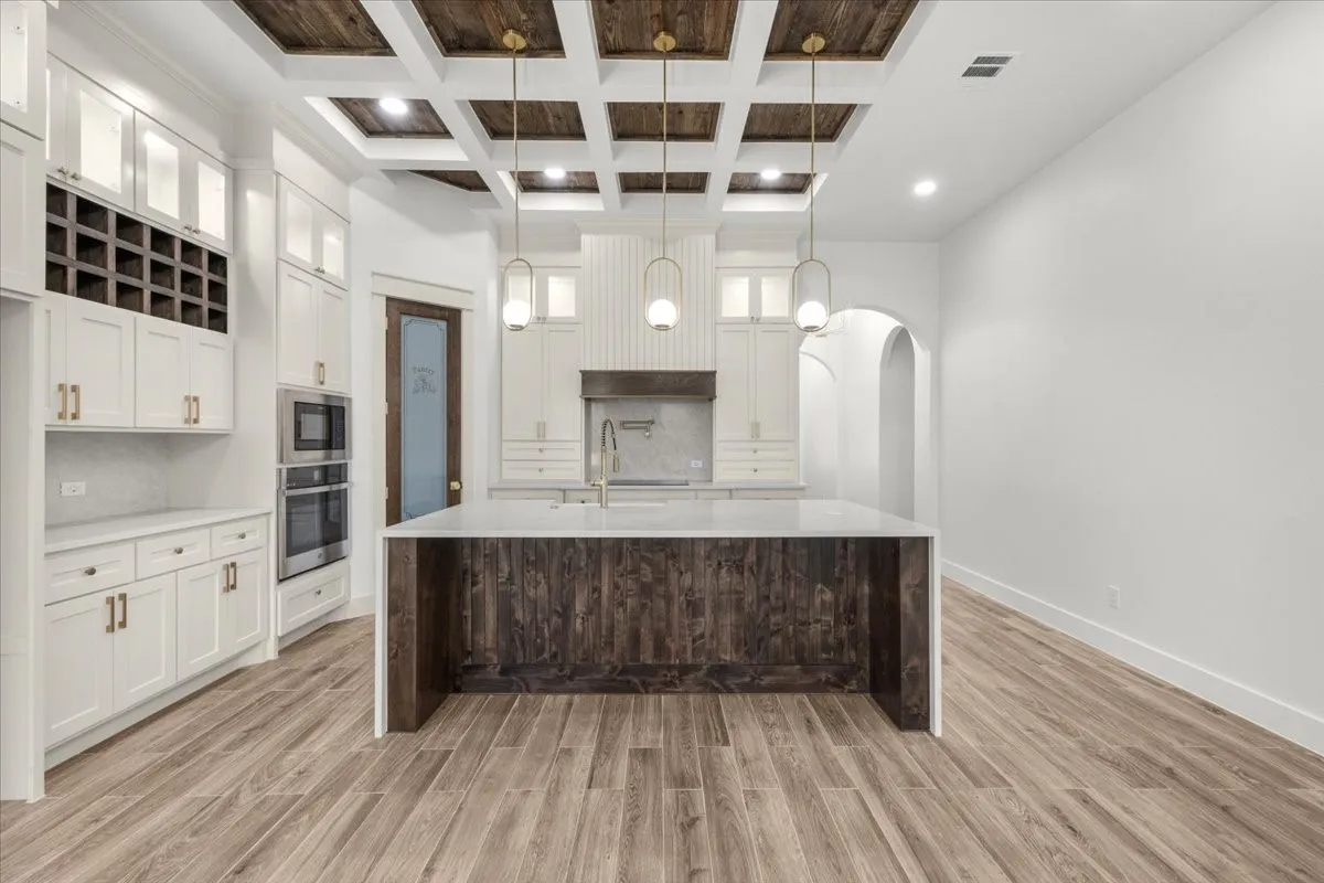 Gourmet kitchen featuring a coffered ceiling with wood-finish panels, integrated stainless steel appliances, a center island with a light-toned countertop, and abundant white cabinetry with gold-tone hardware