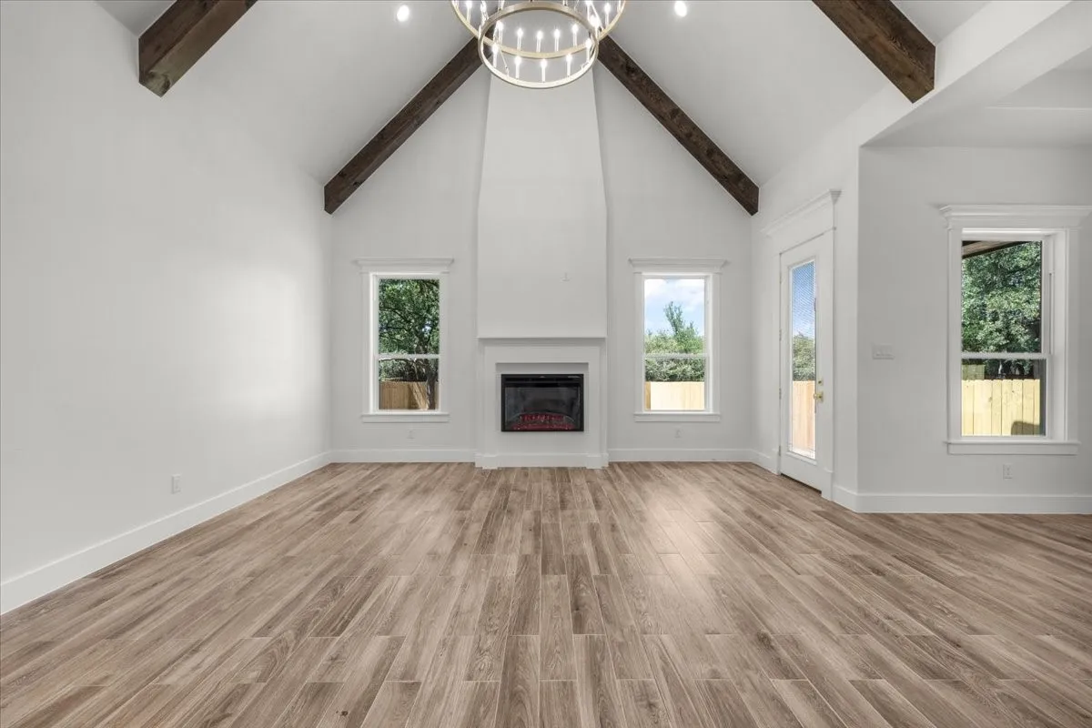 Vaulted ceiling with exposed wood beams, wood-finish flooring, fireplace, recessed lighting, and a contemporary chandelier
