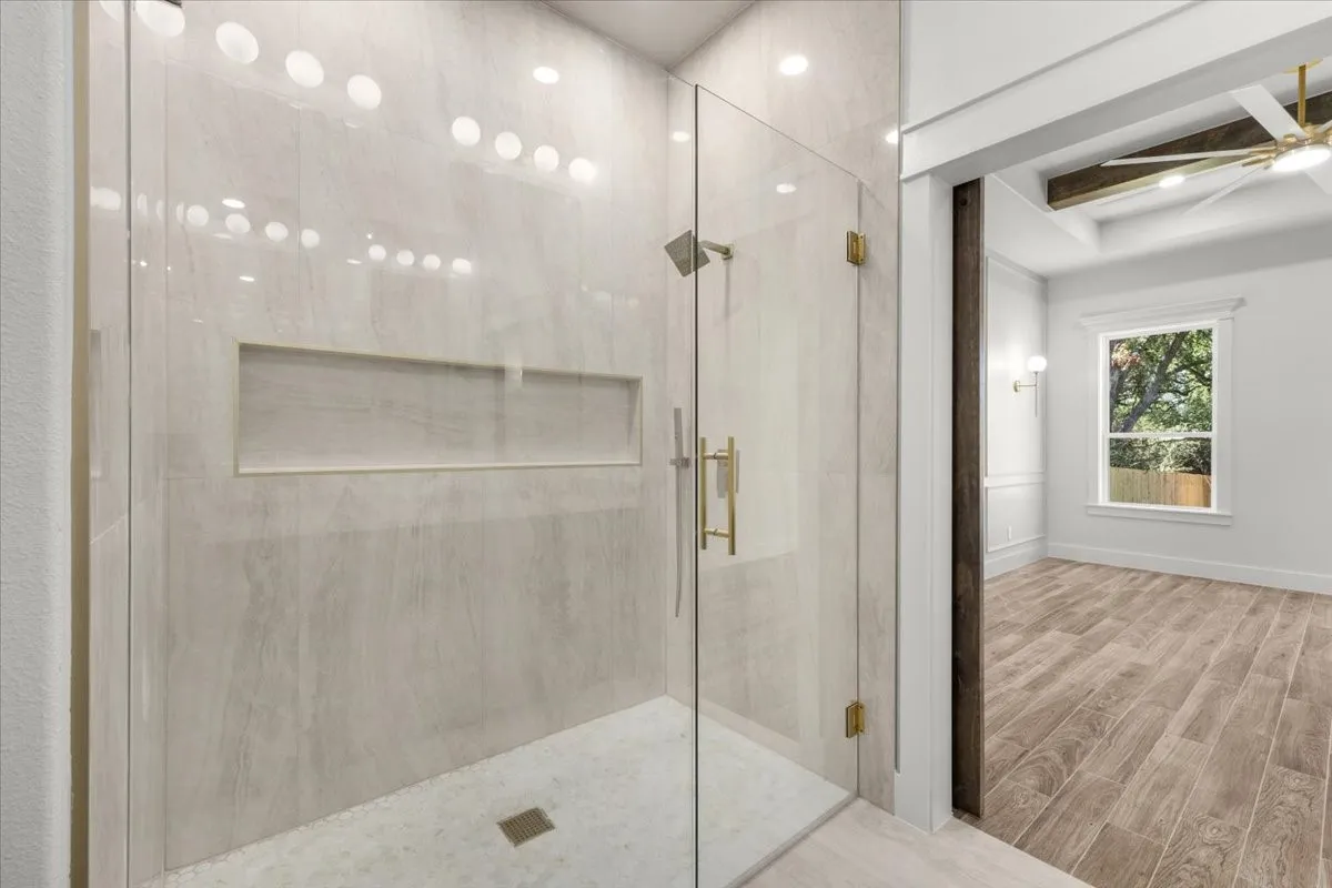 Glass-enclosed shower with a recessed shelf, gold-finish hardware, and a rainfall showerhead