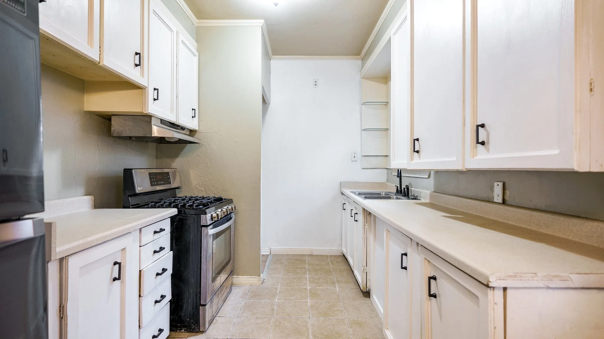 White cabinetry with black hardware, stainless steel gas range, dual basin sink with gooseneck faucet, light-toned countertops, and tile flooring