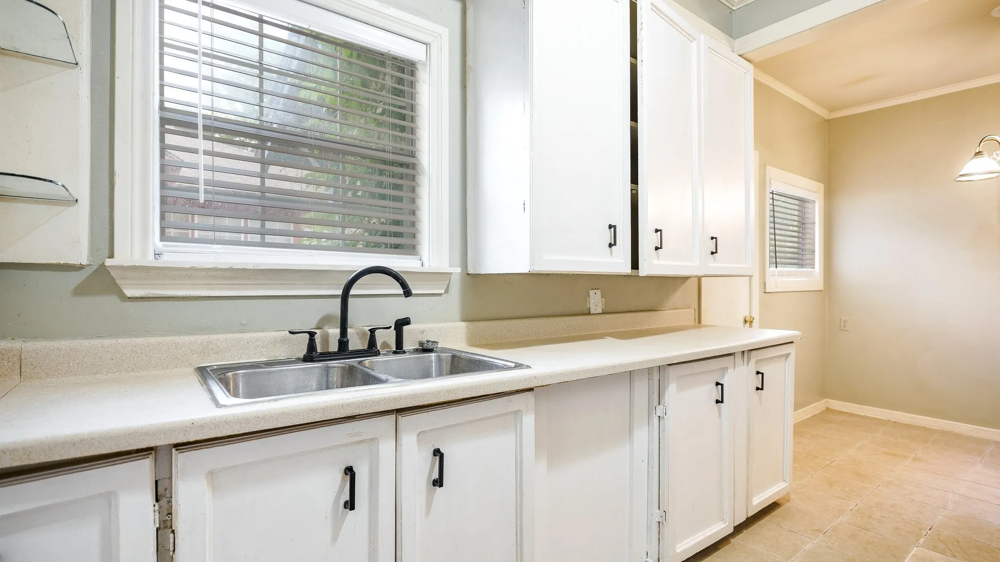 Double basin stainless steel sink with matte black faucet, white cabinetry with black hardware, and light-colored countertops