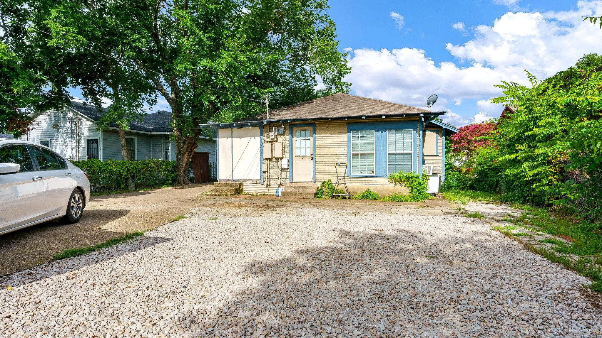 Gravel driveway, single-story residence with light-colored siding, blue window trim, and a composition shingle roof
