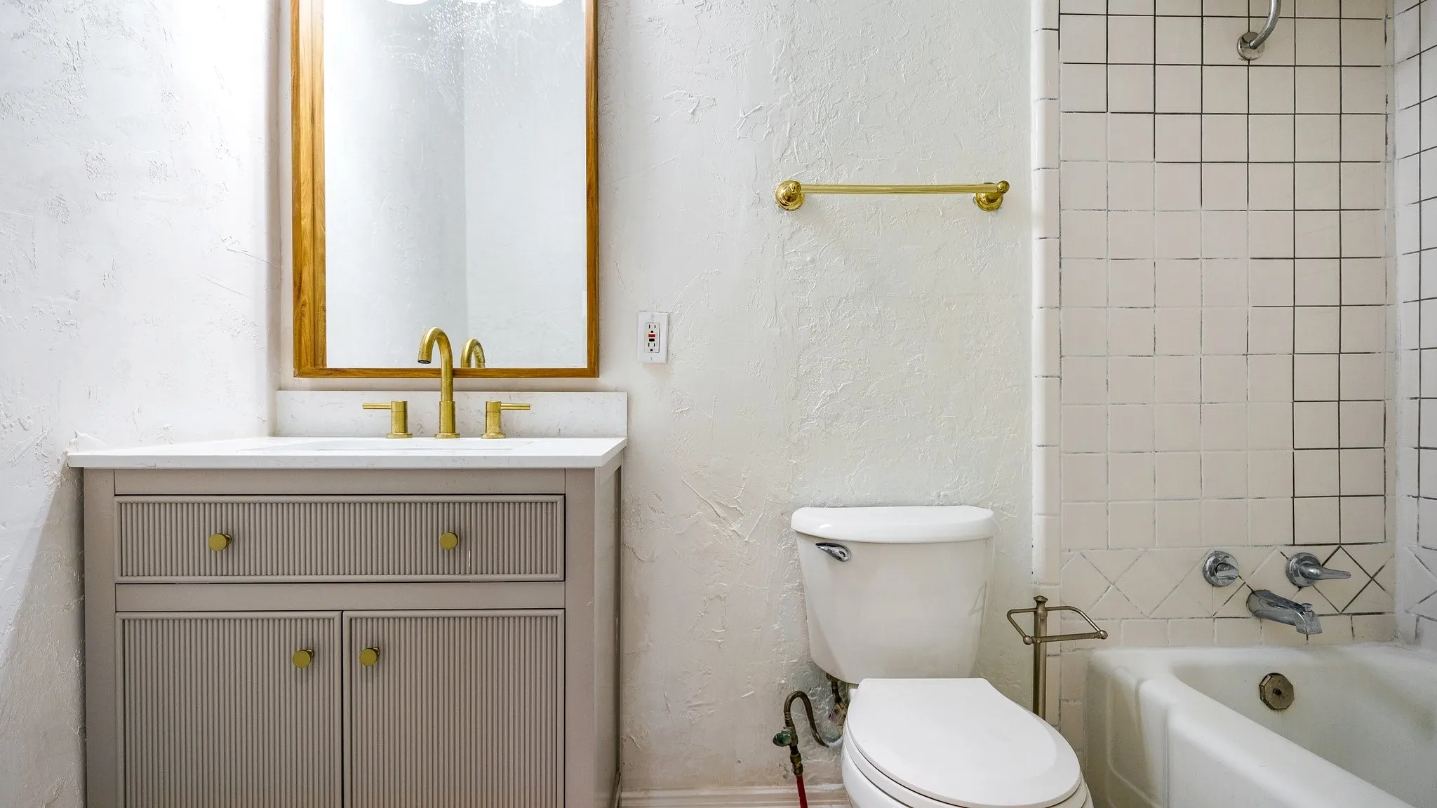 Vanity with fluted drawer and cabinet fronts, gold-toned hardware, white countertop, and brass-framed mirror