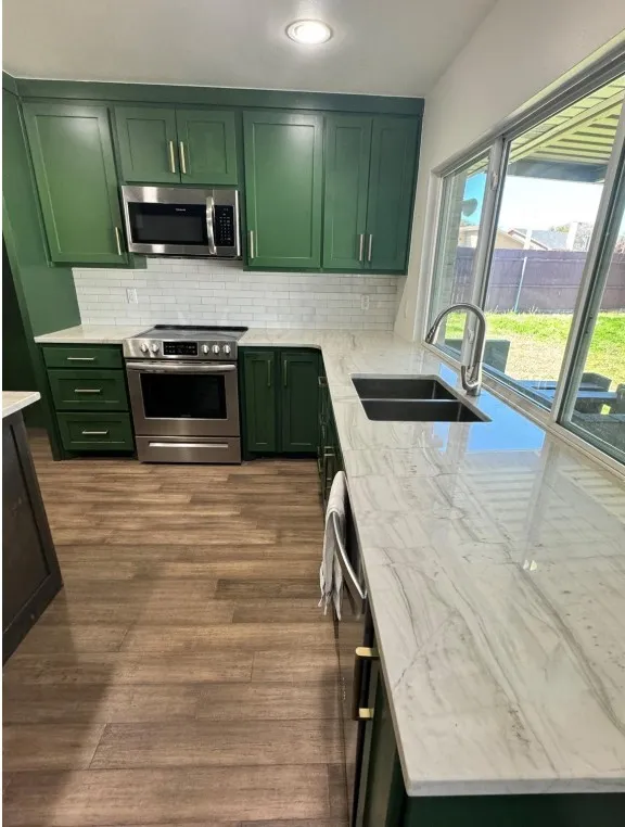 Kitchen featuring green cabinetry, stainless steel appliances, white subway tile backsplash, light-toned countertops, and wood-finish flooring