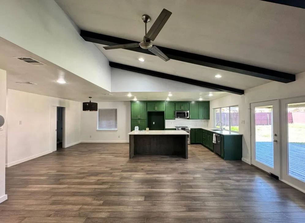 Vaulted ceilings with exposed beams, wood-finish flooring, recessed lighting, and kitchen featuring dark green cabinetry and an island