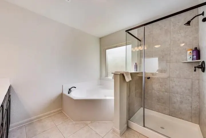 Walk-in shower with tiled walls and glass enclosure, separate corner soaking tub, ceramic tile flooring, and a window with privacy glass