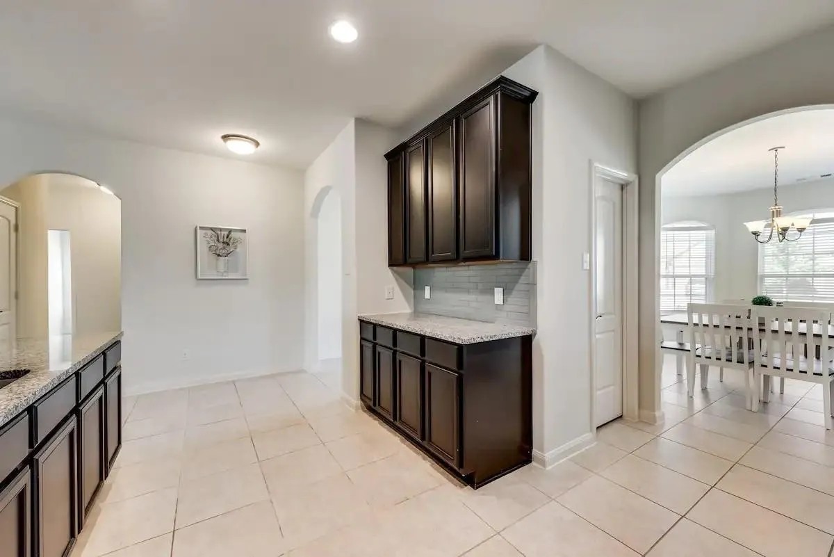 Dark wood-finish cabinetry, light-toned tile flooring, granite-style countertops, and a subway tile backsplash