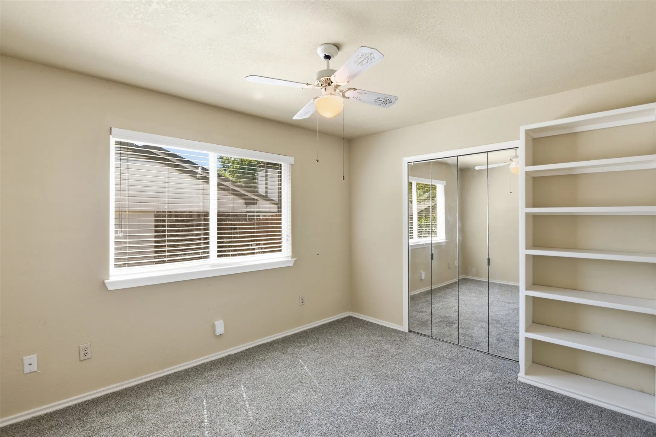 Light neutral wall color, built-in shelving, mirrored closet doors, ceiling fan, and carpet flooring