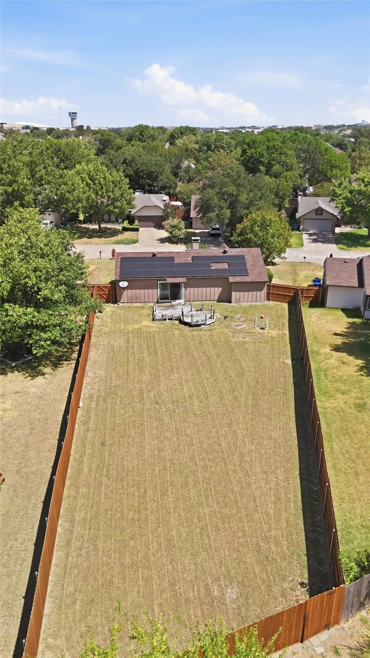 Expansive fenced yard with a manicured lawn, a brown-sided residence, a deck, and solar panels