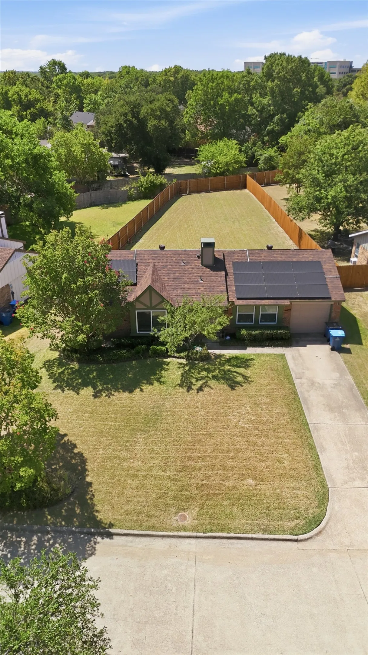 House with a brown shingle roof, solar panels, and a landscaped front yard