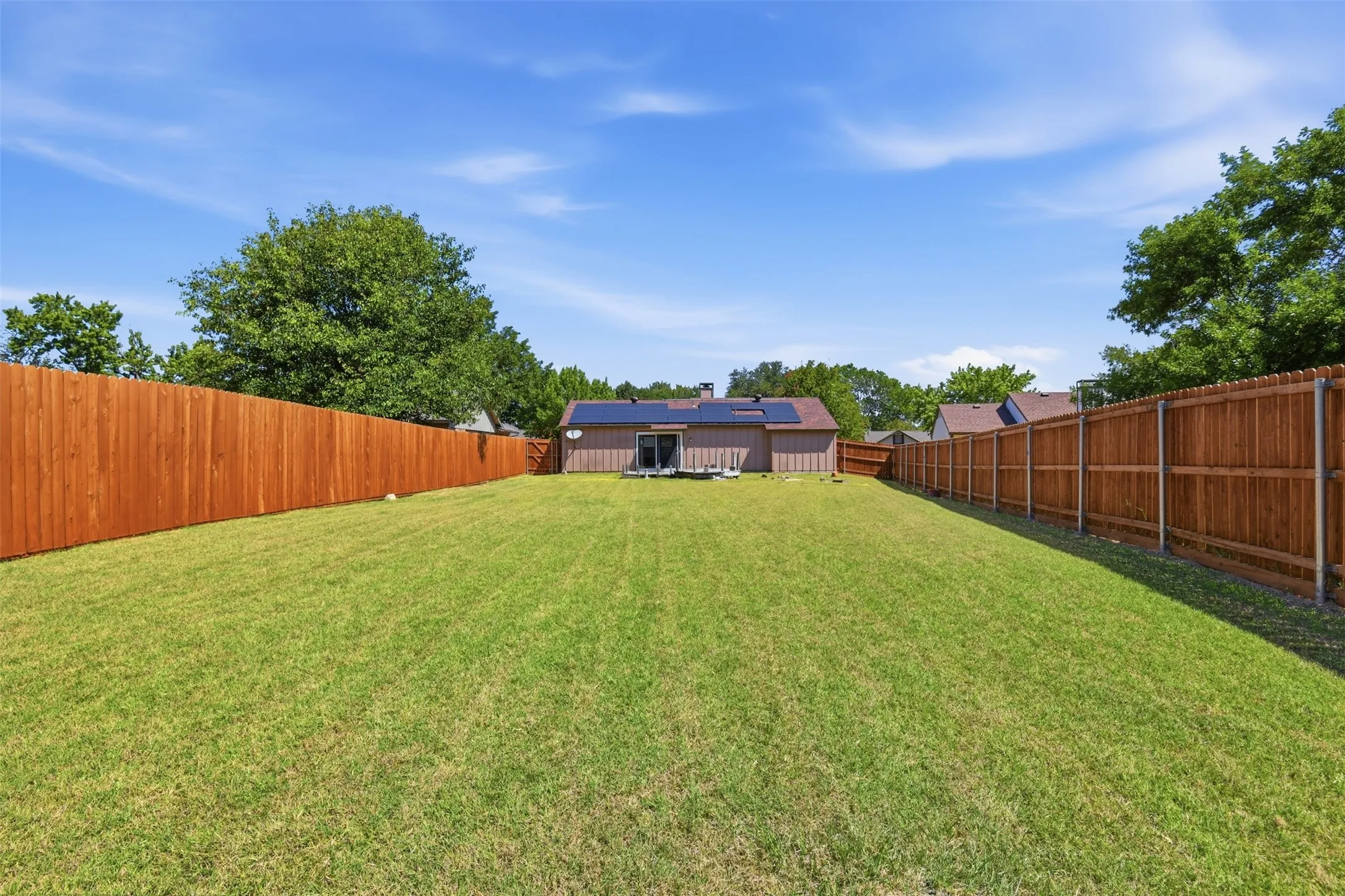 Expansive backyard featuring a manicured lawn, full privacy fencing, and mature trees