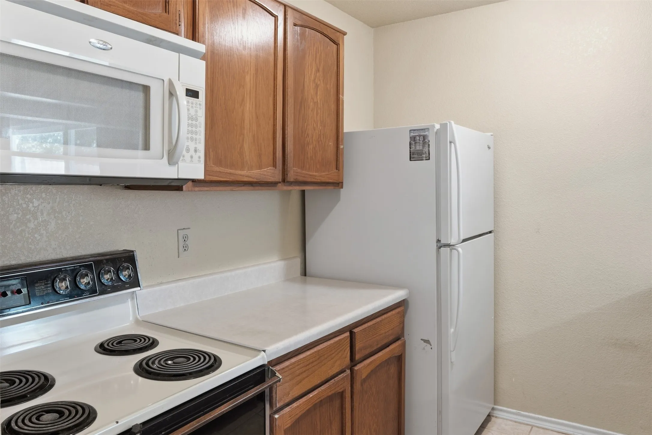 Kitchen featuring wood cabinetry, white microwave, white electric range, white refrigerator, and light-colored countertops