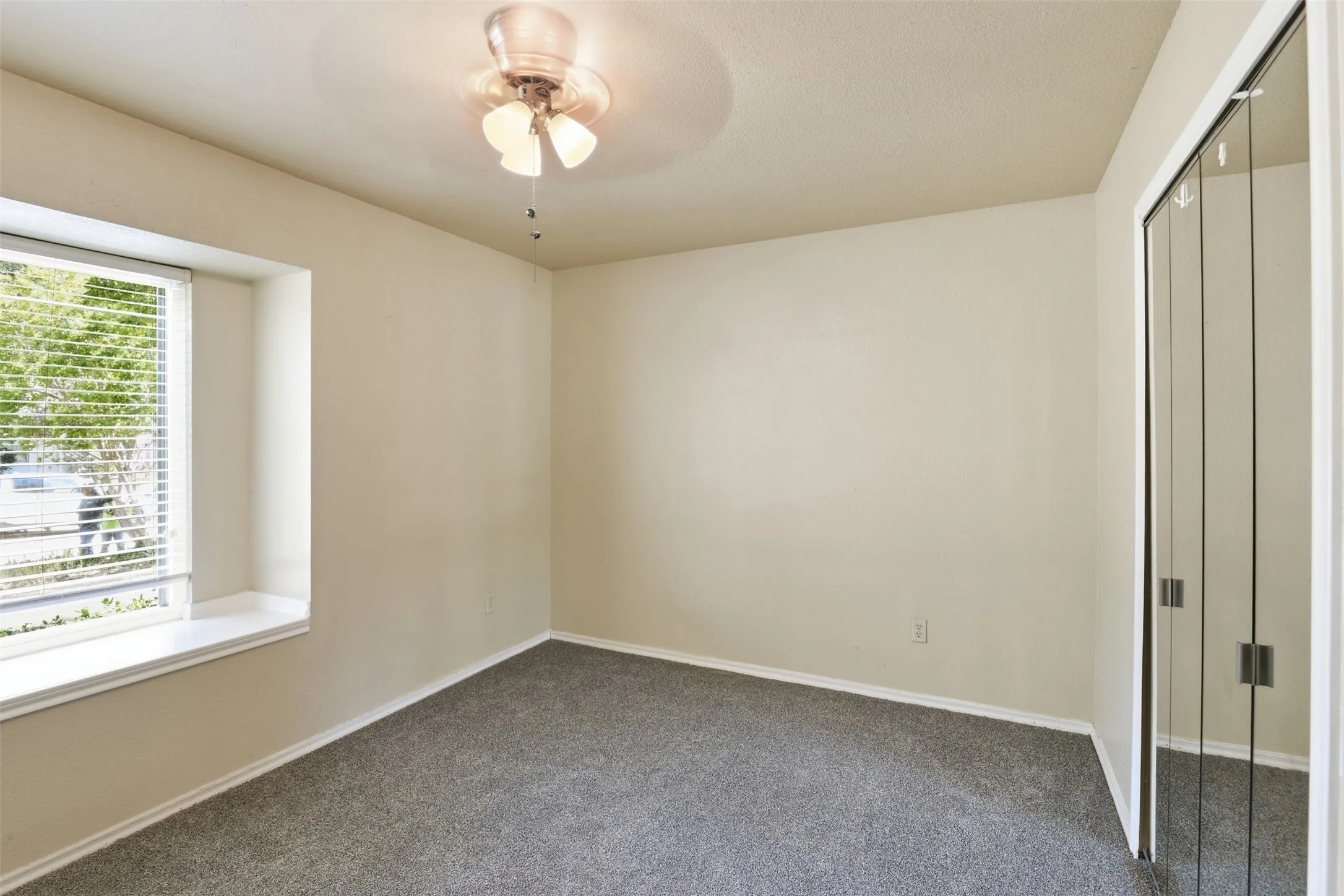 Wall-to-wall carpeting with a built-in window bench, ceiling fan with light fixture, and mirrored closet doors