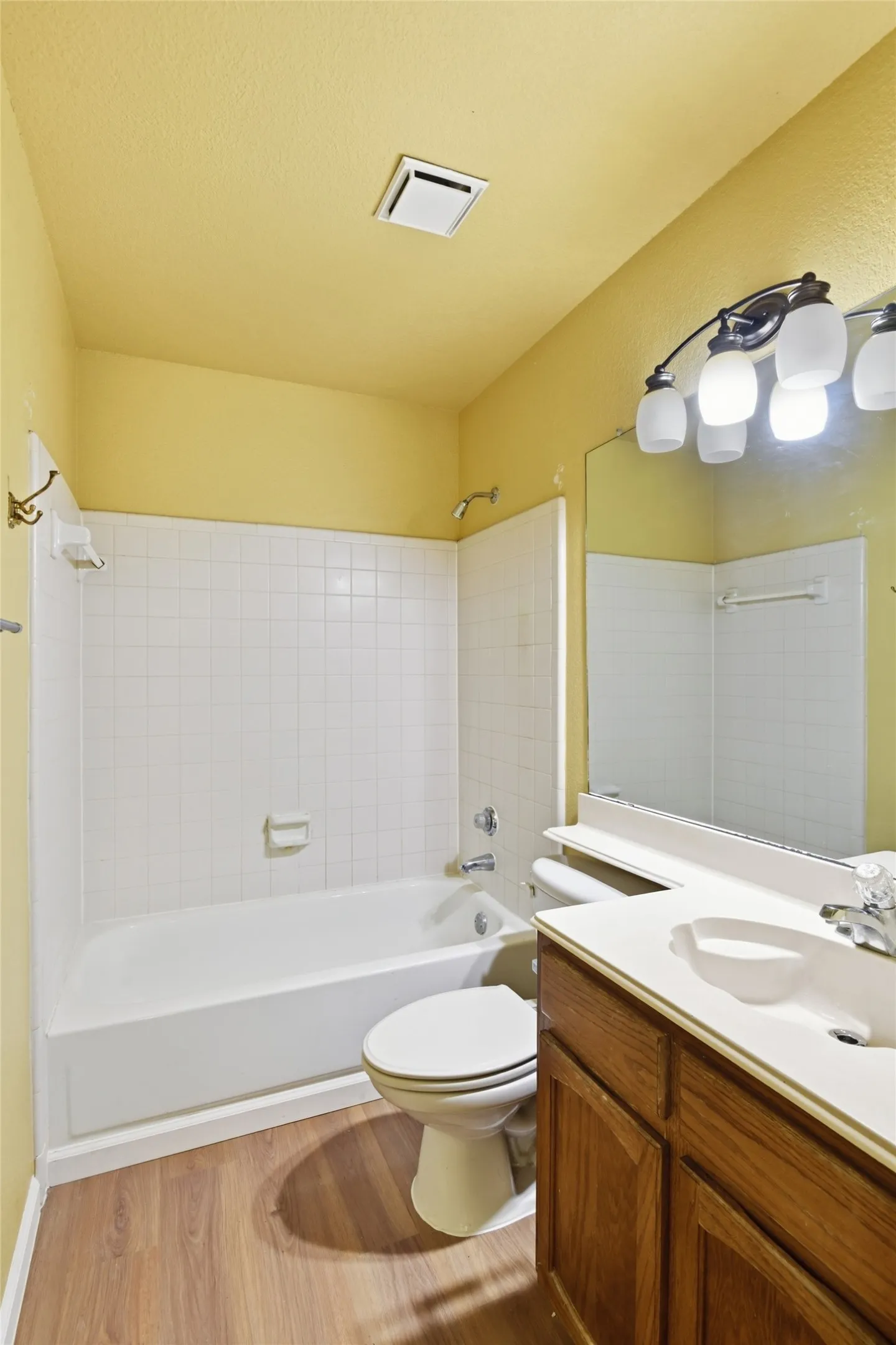 Tub and shower combination with white subway tile surround, wood-finish flooring, and a single vanity with wood cabinetry