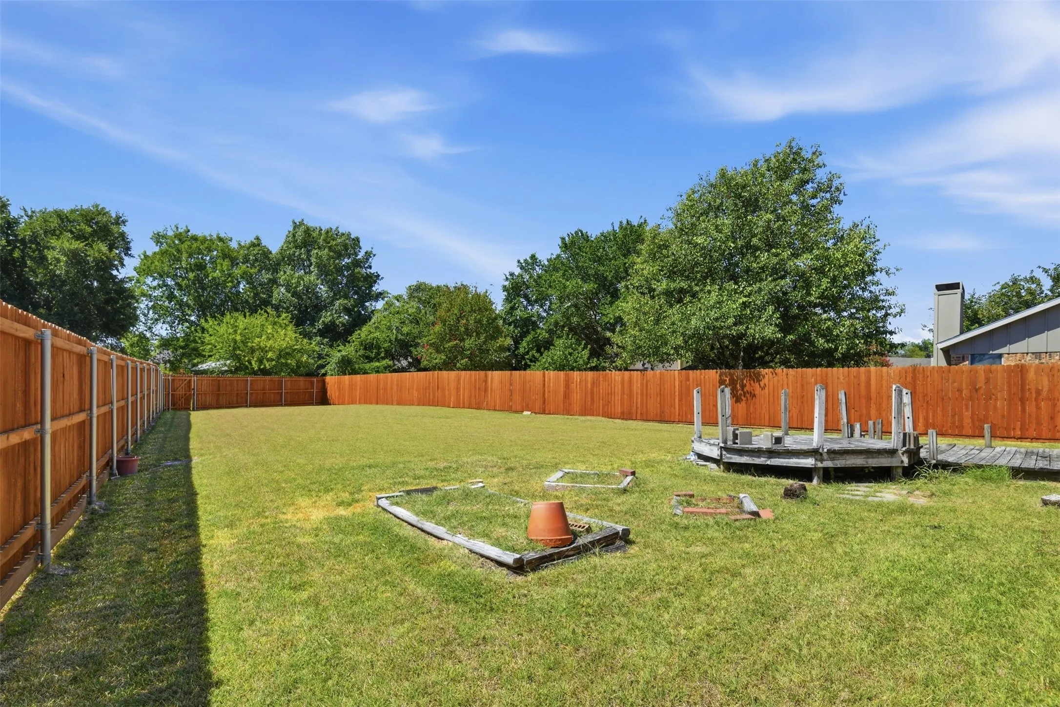 Expansive backyard featuring a wood privacy fence, mature trees, and a raised wood platform