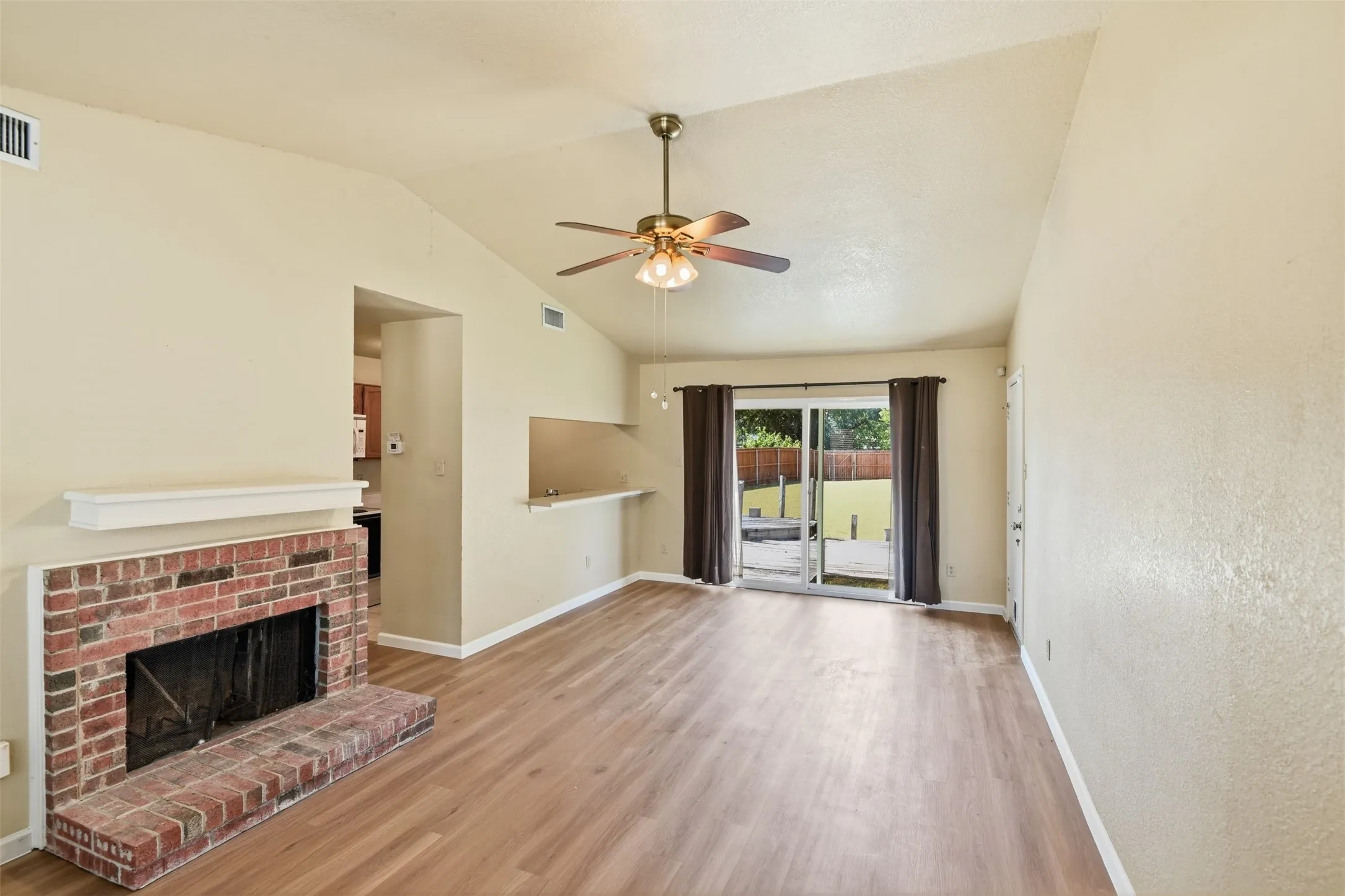 Vaulted ceiling with a ceiling fan, brick fireplace with a white mantel, wood-finish flooring, and a sliding glass door