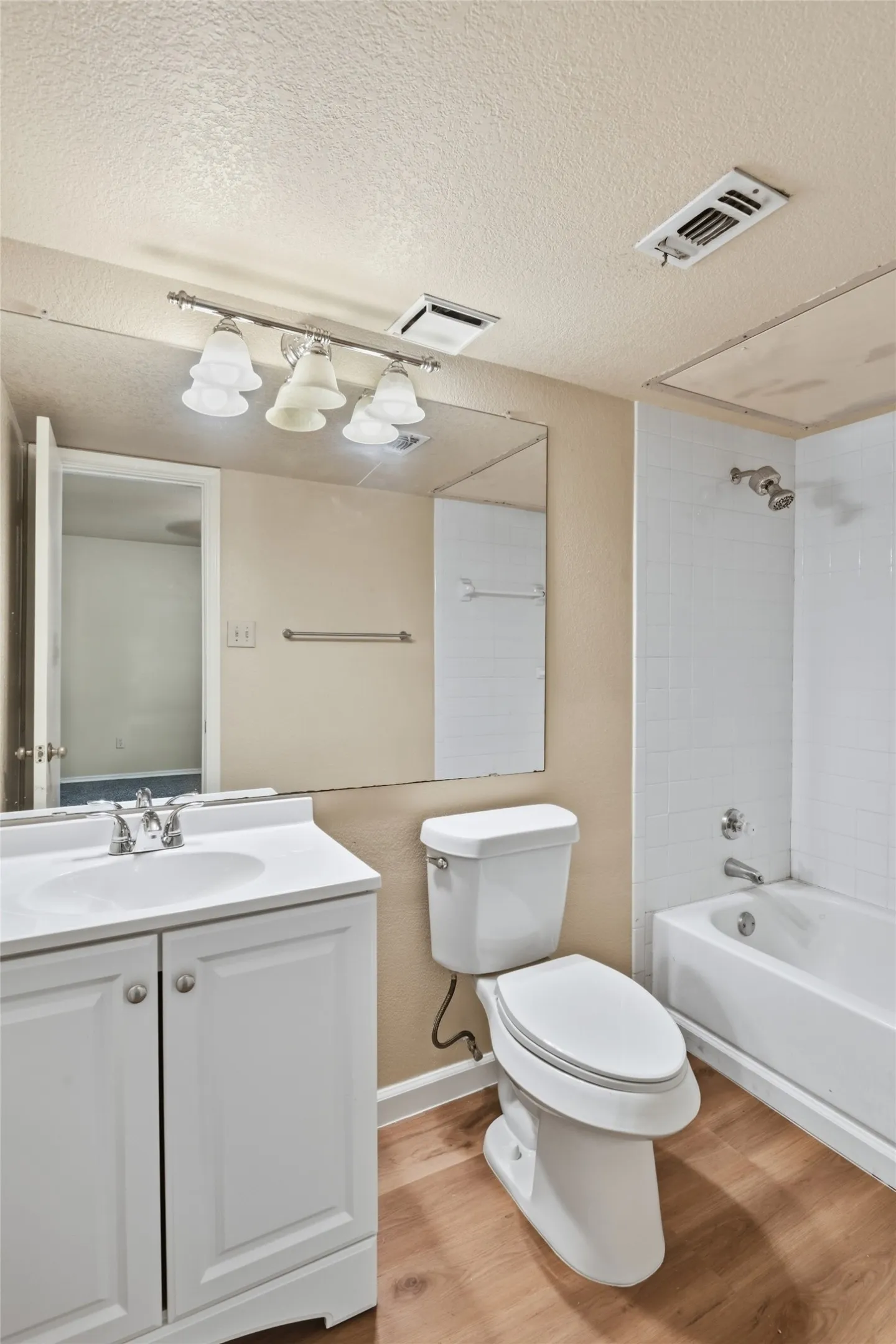 Bathroom featuring a white vanity with integrated sink, chrome faucet, wood-finish flooring, and a white bathtub with tile surround