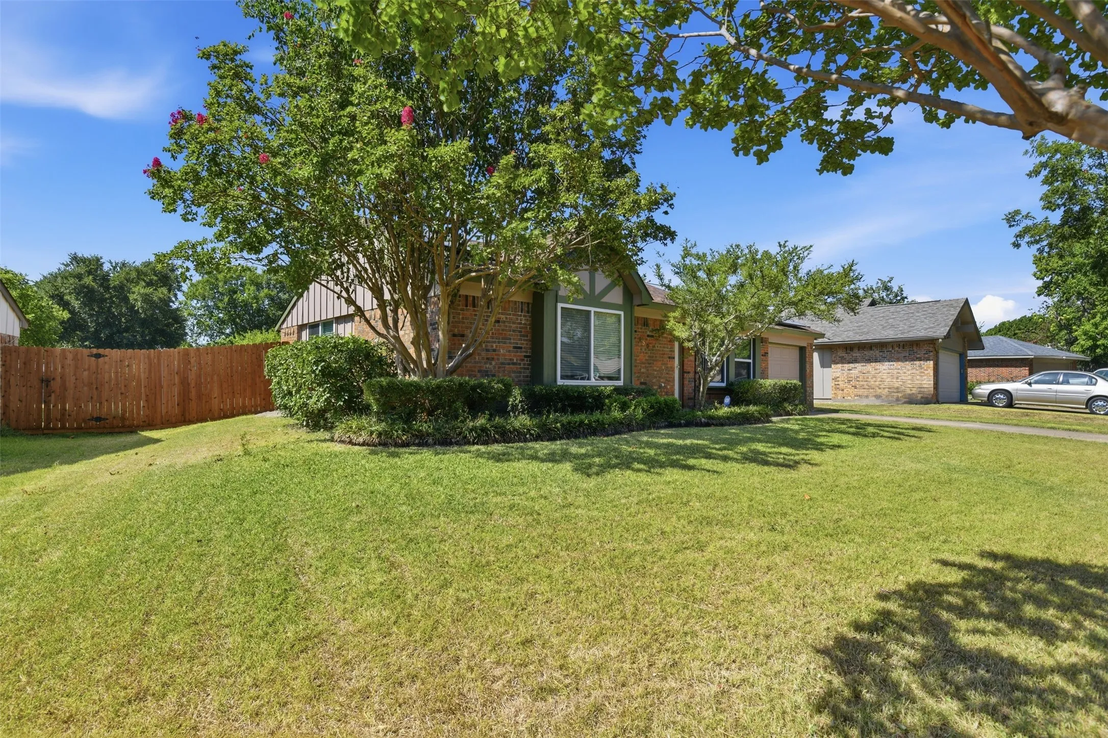 Brick exterior with decorative wood trim, mature trees, established landscaping, and a wood privacy fence