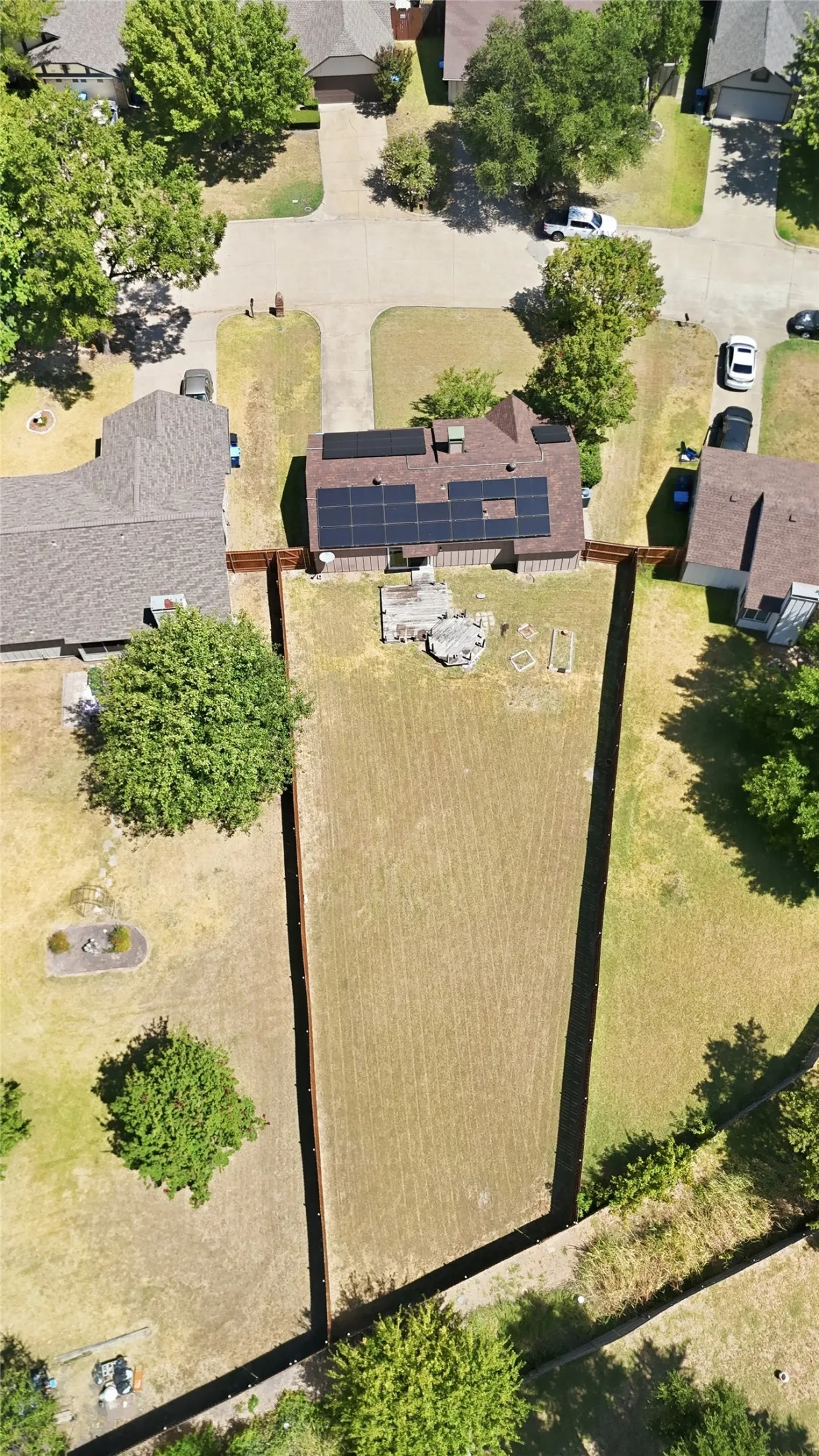 Residential property featuring a shingle roof with solar panels, a fenced backyard, and mature trees