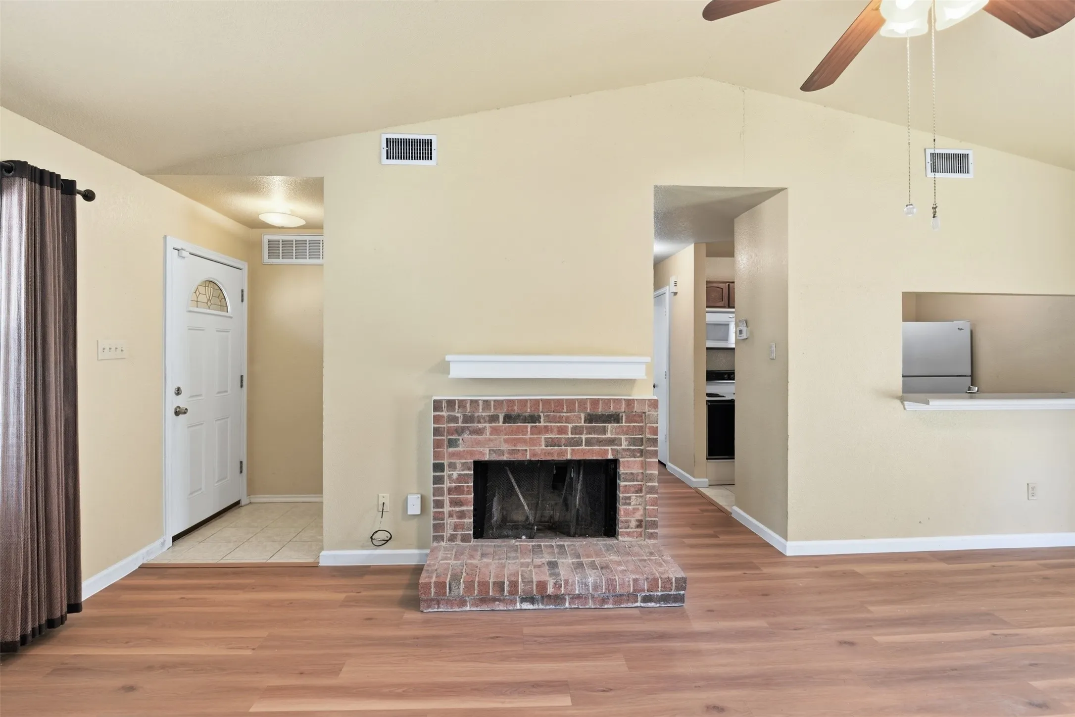 Vaulted ceiling, wood-finish flooring, brick fireplace, ceiling fan, and a breakfast bar
