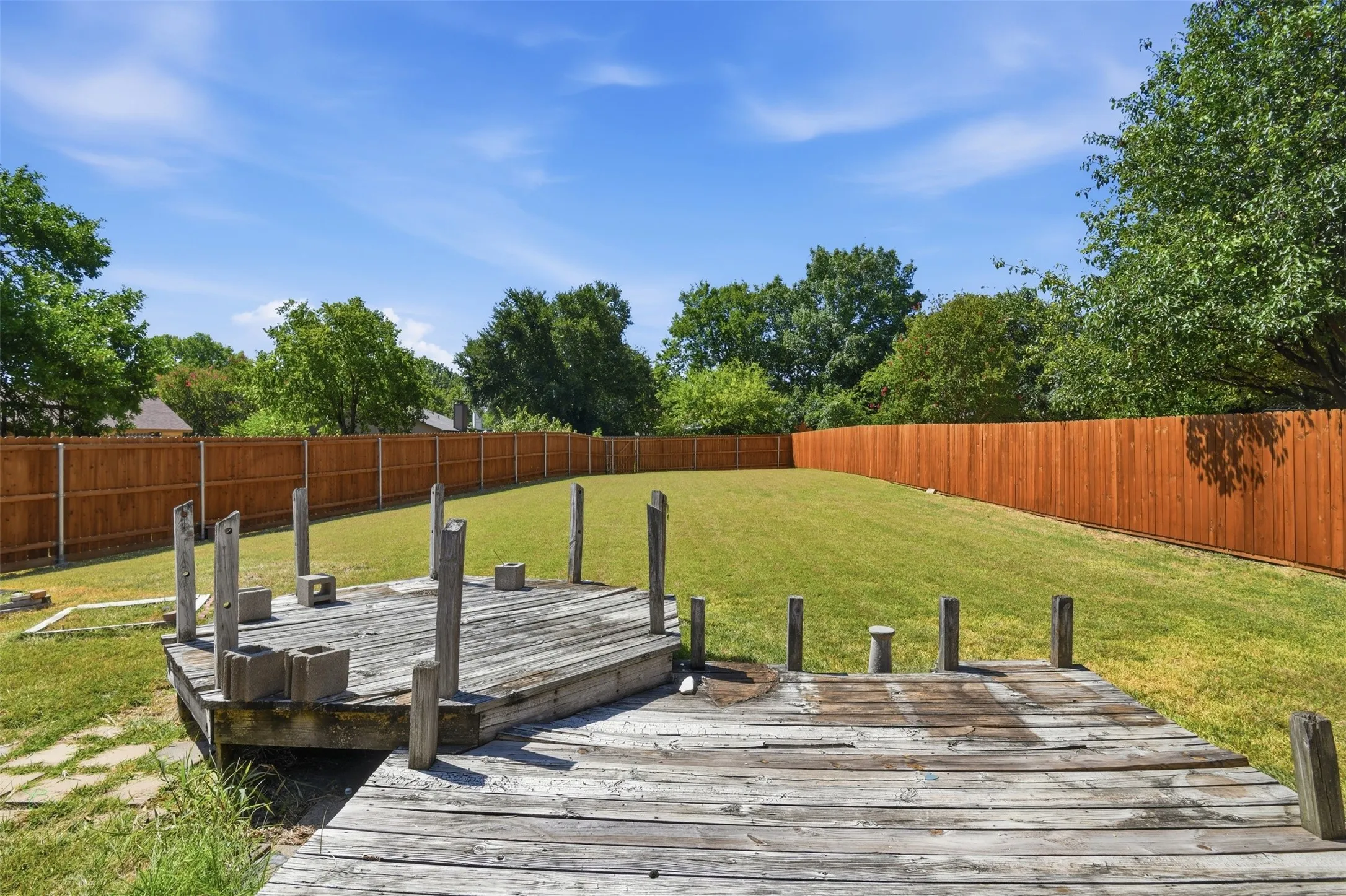 Expansive backyard featuring a large wooden deck, natural wood privacy fencing, and mature perimeter trees