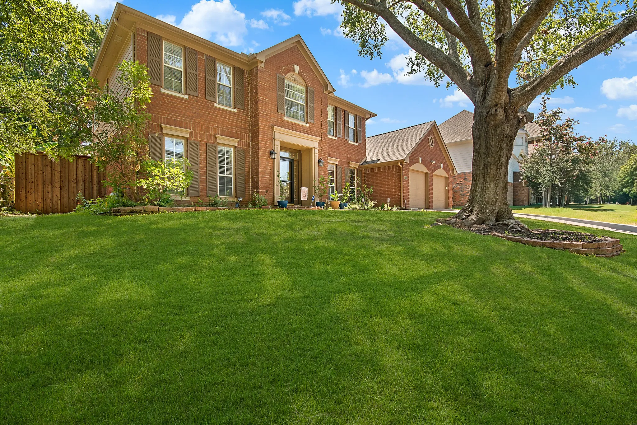 Wood-finish flooring throughout, a door with privacy glass, multiple windows with blinds, a ceiling fan with integrated lighting, and an adjacent brick fireplace