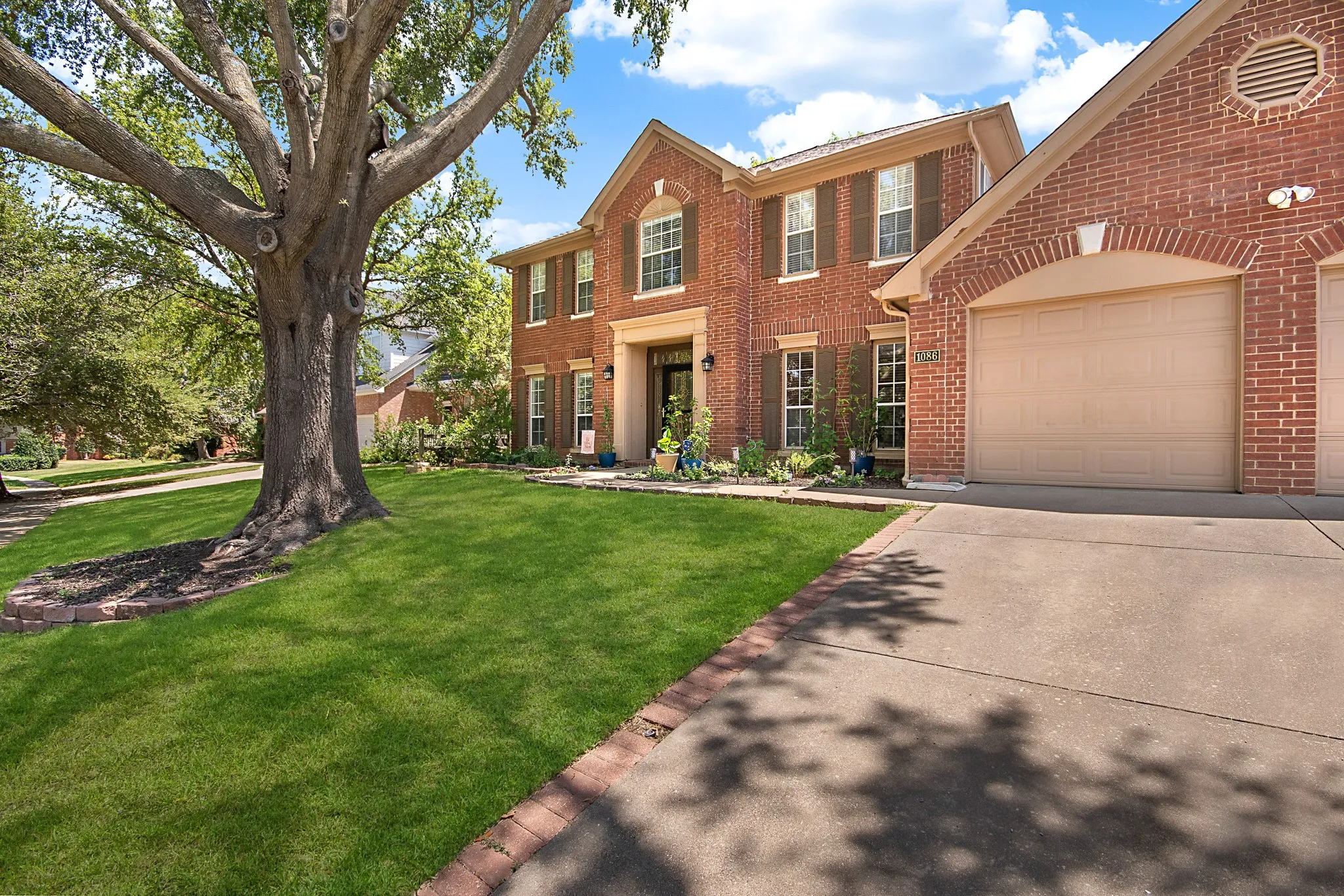 Brick exterior with a large mature tree, green lawn, and a two-car garage