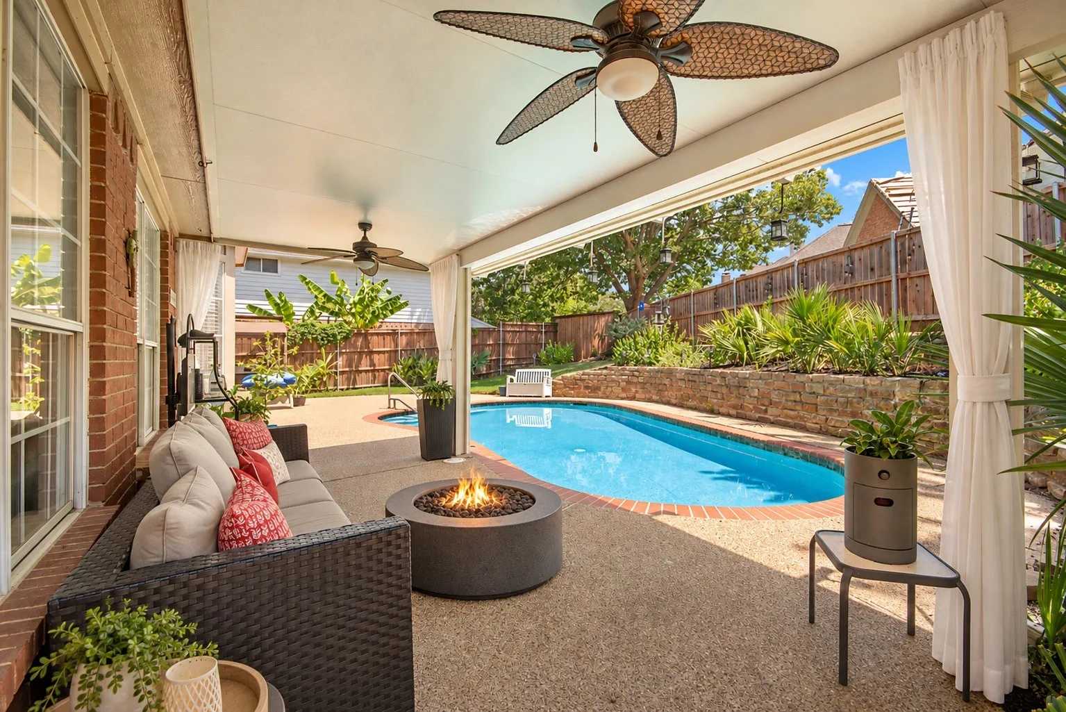 Covered patio featuring an in-ground swimming pool, stone retaining wall, and two ceiling fans