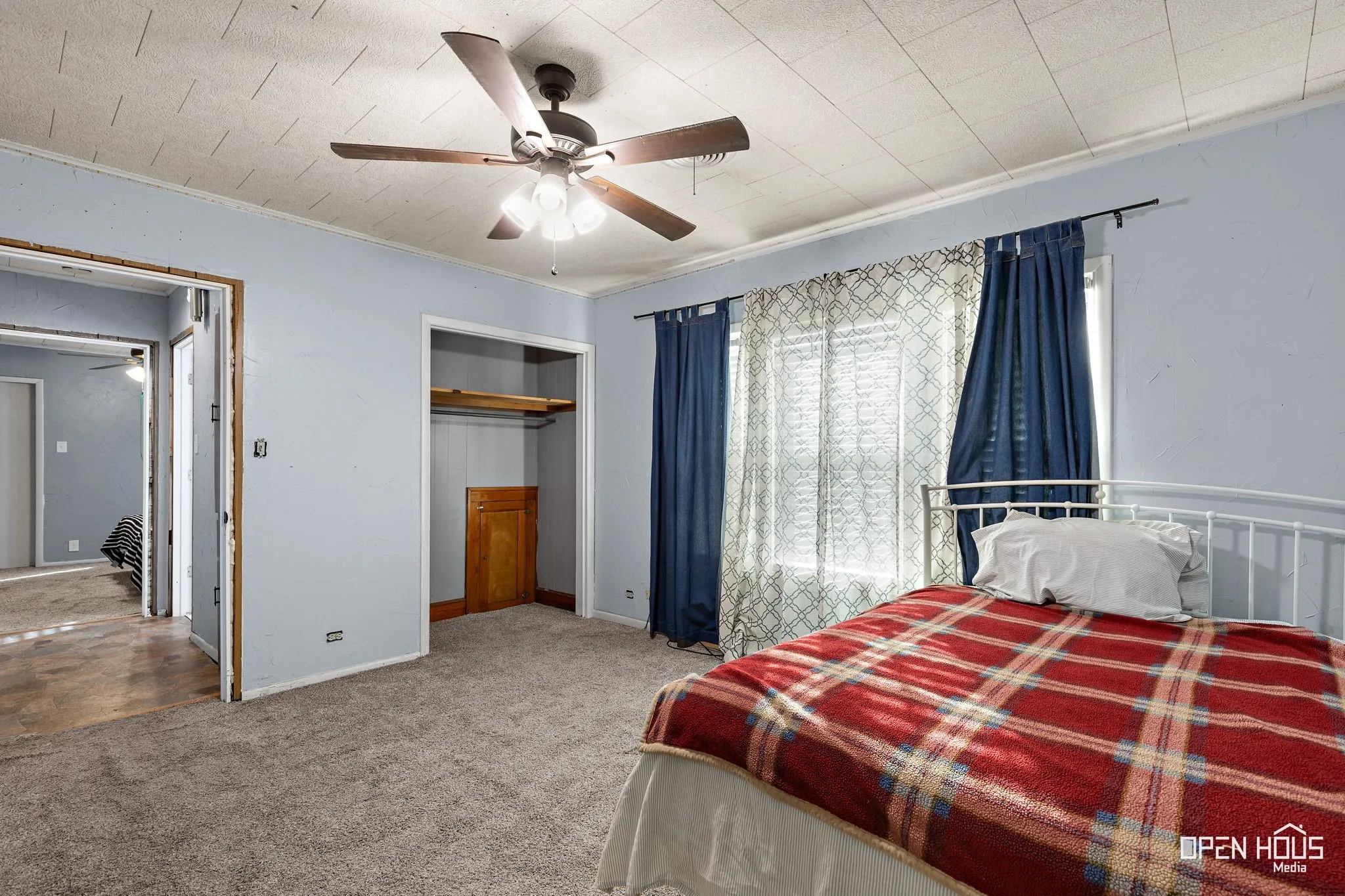 Carpeted flooring, ceiling fan with integrated lighting, window with curtain rods, and an open closet space with a wooden shelf