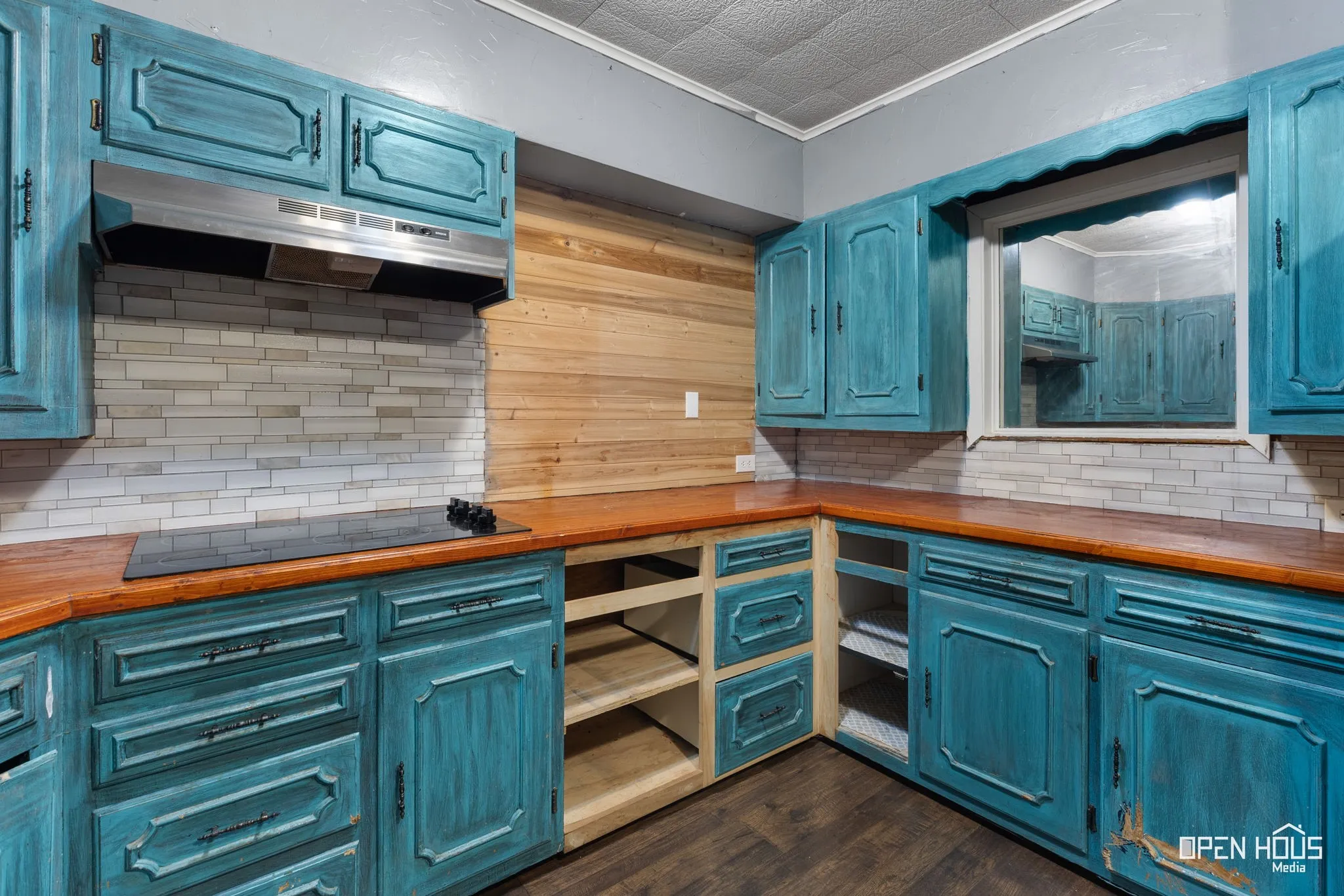 Kitchen featuring teal cabinetry, wood-finish countertops, stainless steel range hood, and a light-toned tile backsplash