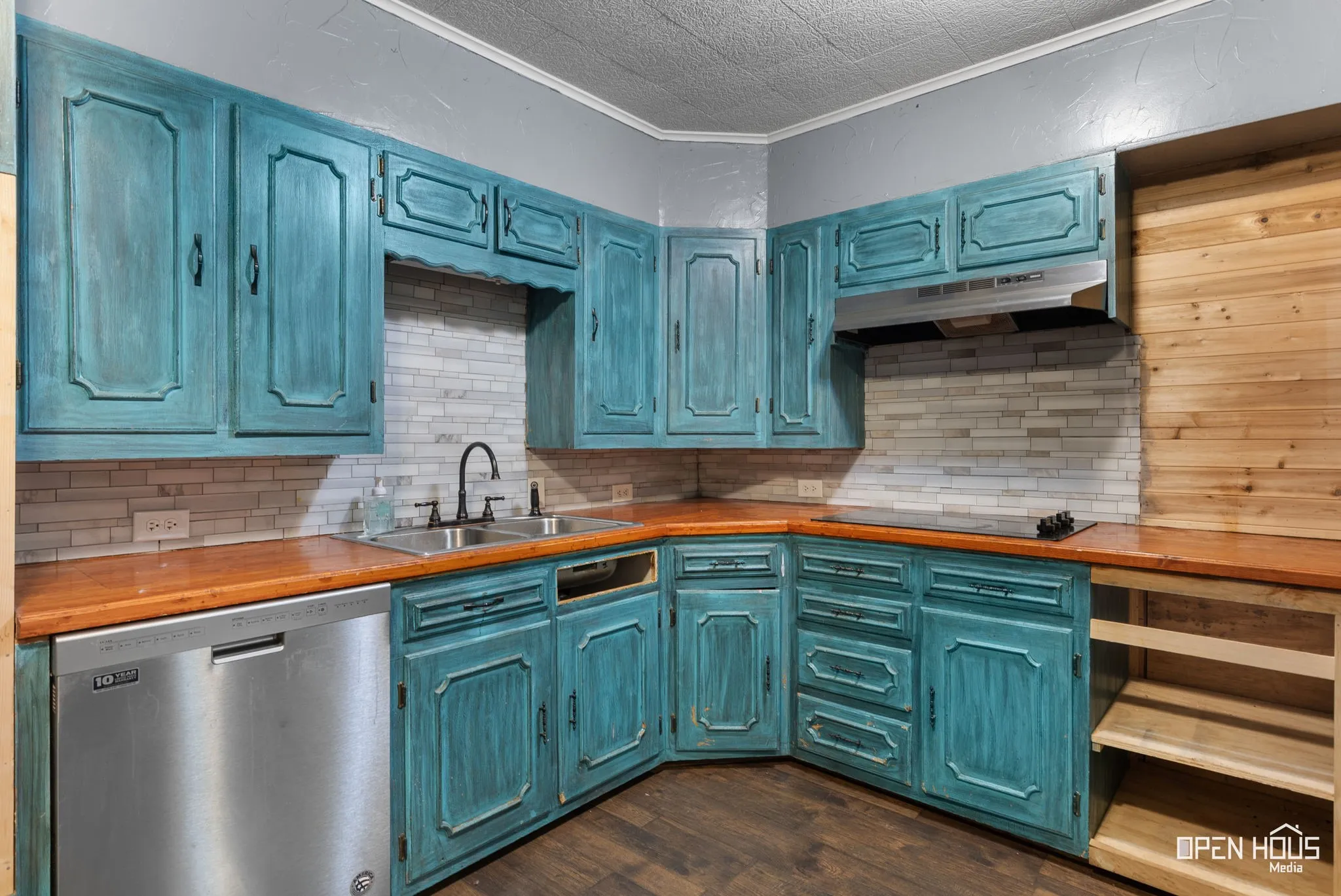 Corner kitchen featuring teal-finished cabinetry, wood-finish countertops, stainless steel appliances, and a tiled backsplash