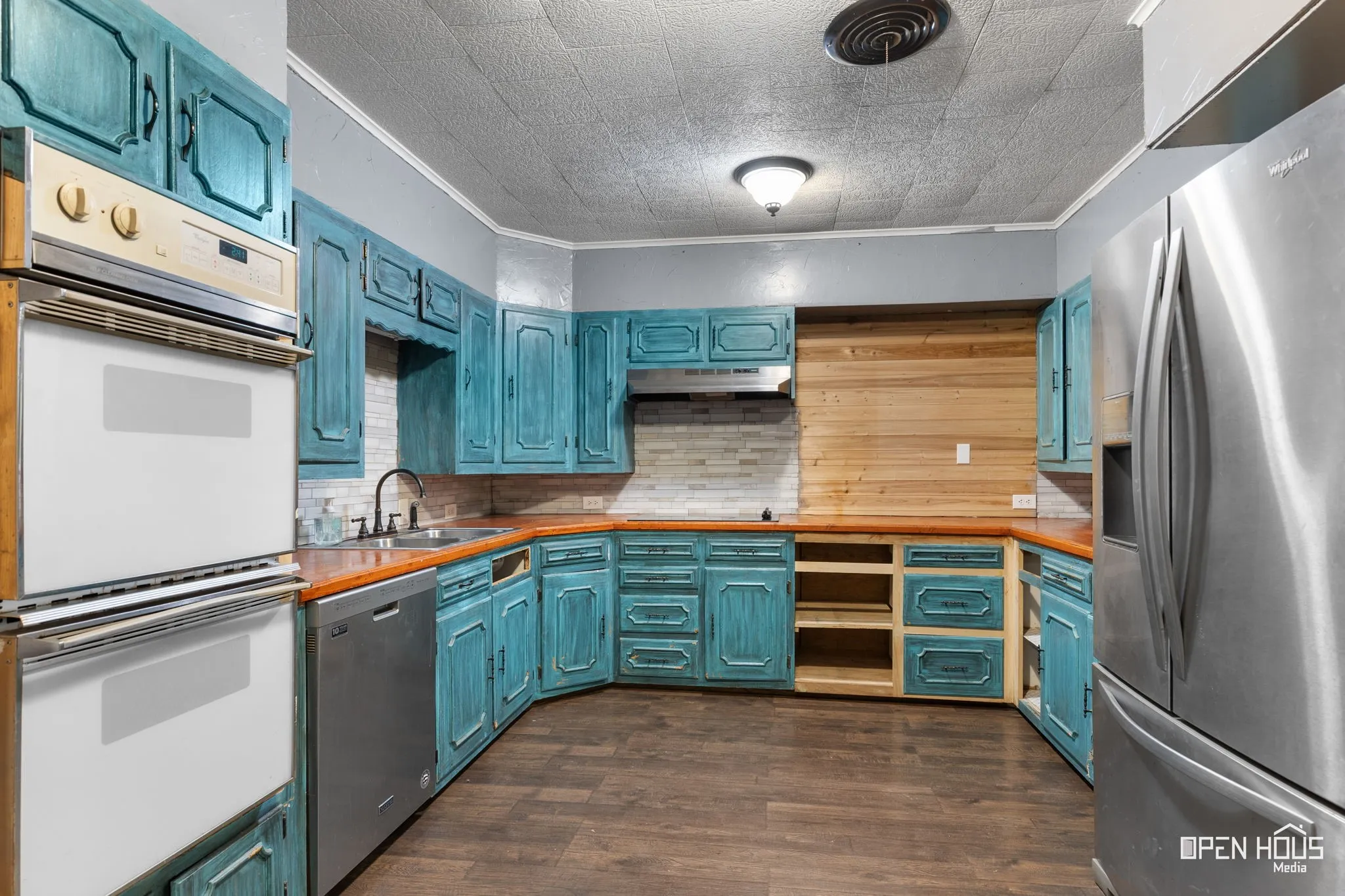 Kitchen with wood-finish flooring, teal cabinetry, wood countertops, and stainless steel appliances