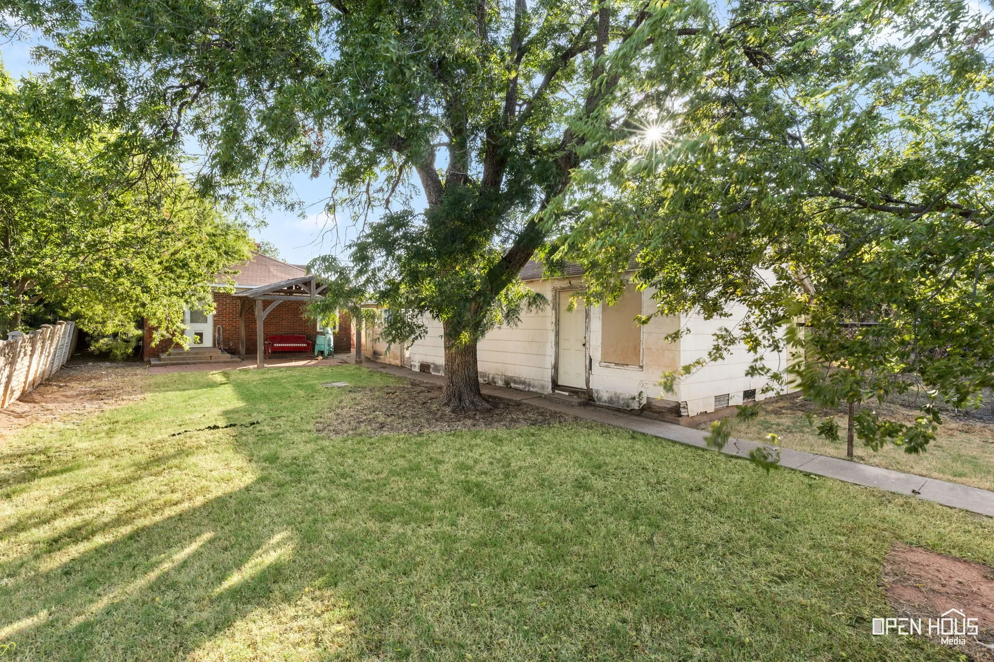Expansive lawn area with mature trees, brick exterior, and a wood pergola