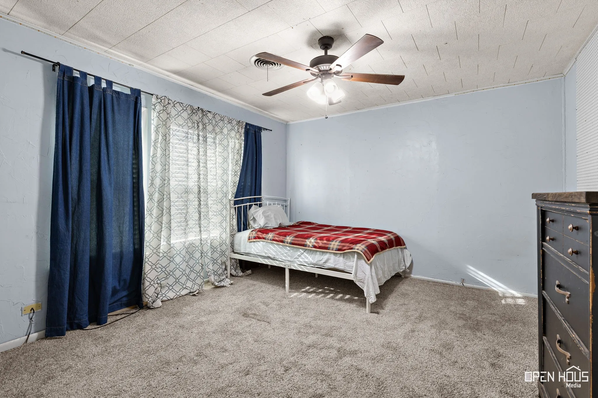 Wall-to-wall carpeting, window with layered curtains, ceiling fan, and textured ceiling