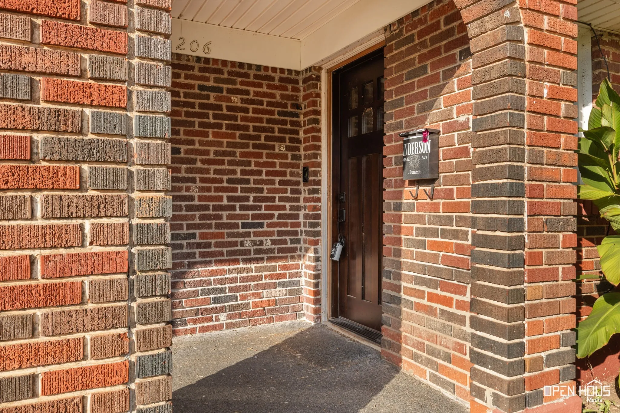 Brick exterior featuring a wood-paneled entry door, concrete porch, and integrated mailbox