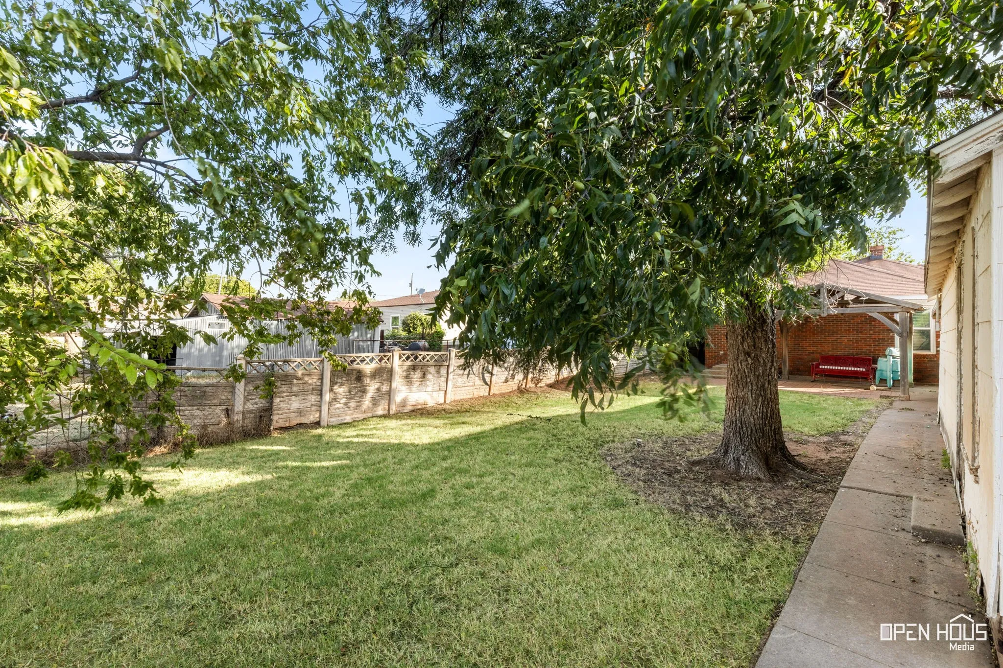 Expansive yard featuring mature trees, a concrete walkway, and a covered patio with brick siding