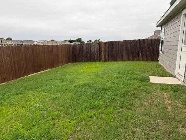 Private backyard featuring a wood privacy fence, a concrete pad, and a light-colored exterior wall with a white door