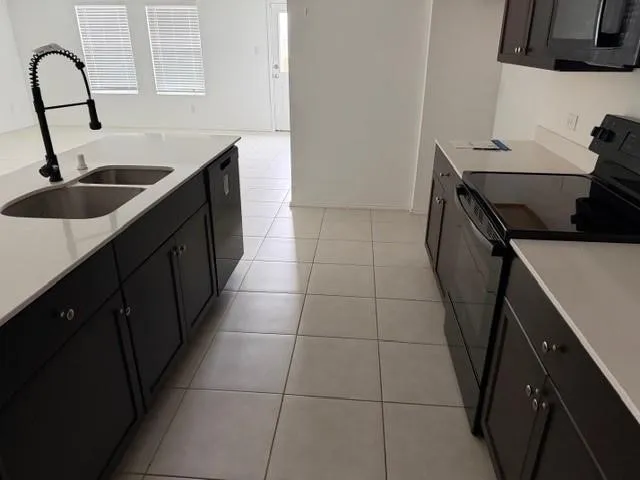 Kitchen featuring a center island, dual basin sink, black pull-down faucet, white countertops, and dark cabinetry