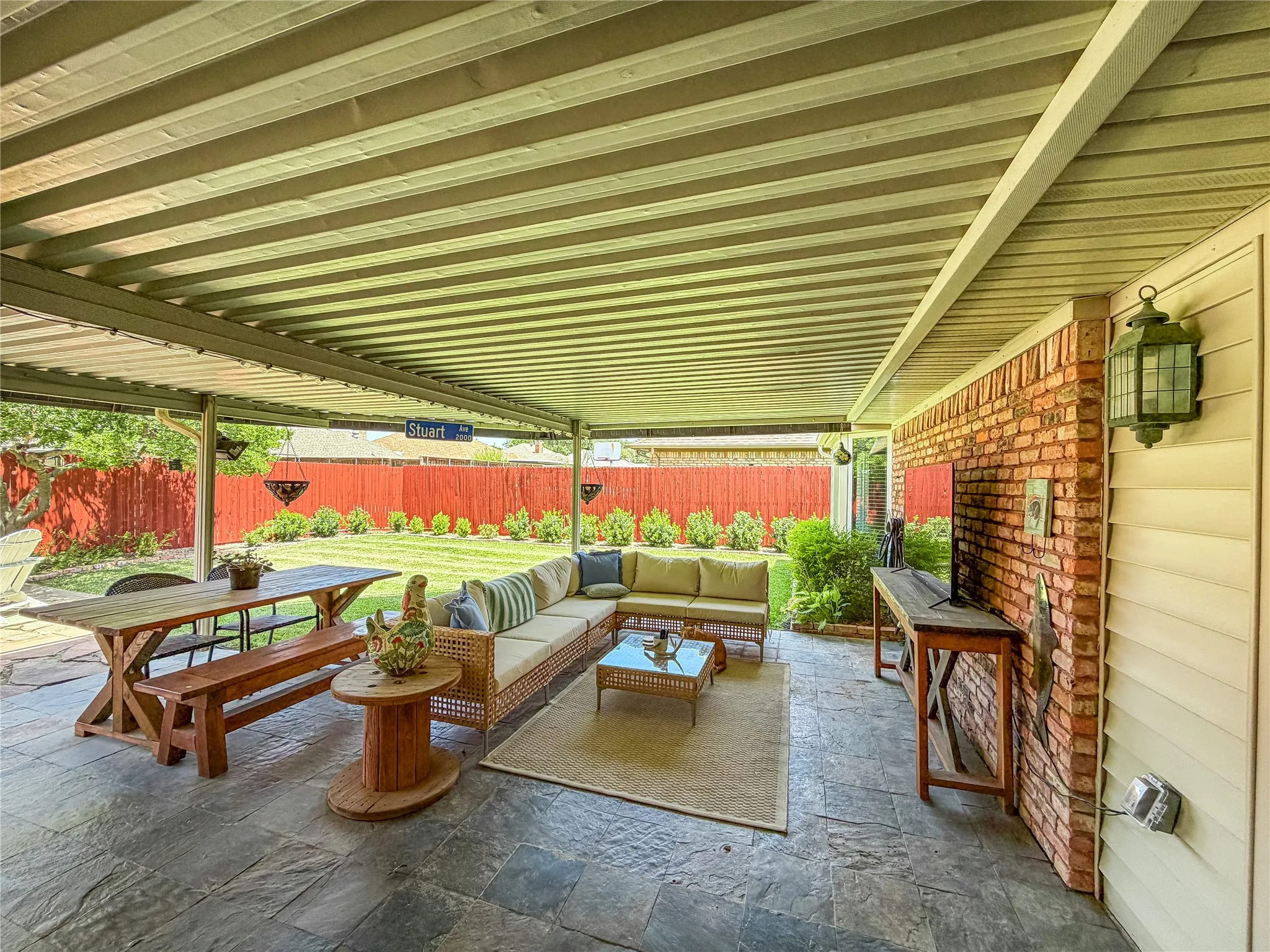 Covered patio with flagstone flooring, brick accent wall, and a manicured lawn