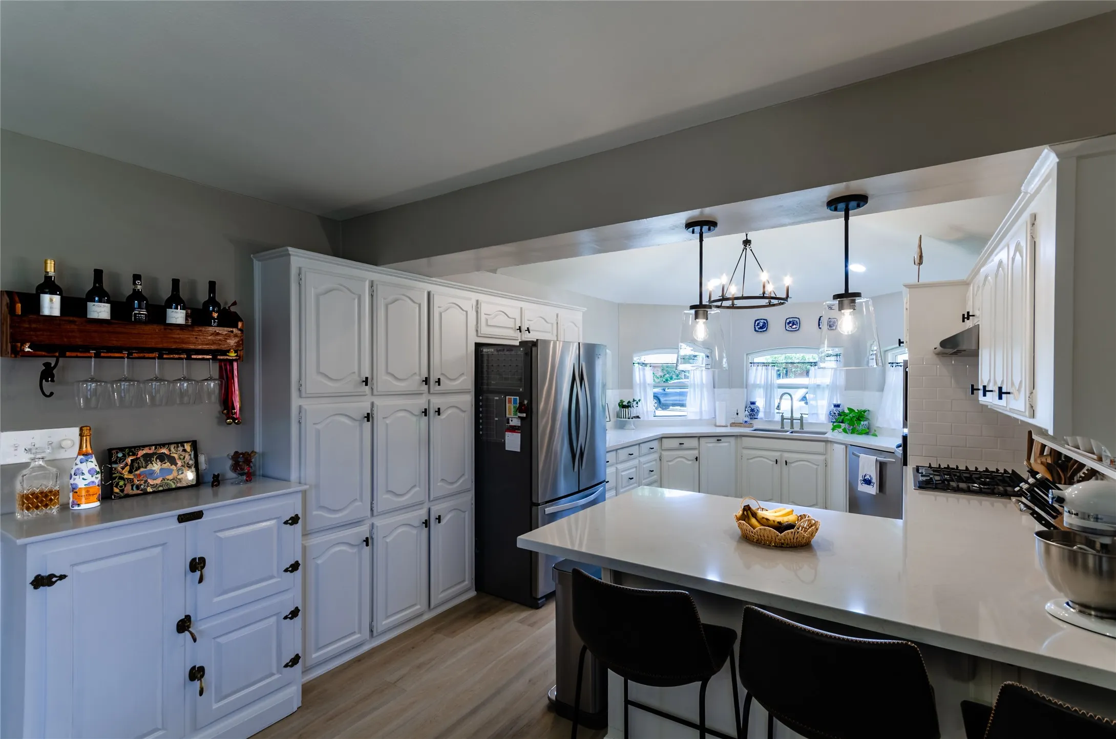 White cabinetry, wood-finish flooring, stainless steel appliances, white subway tile backsplash, and light-toned countertops