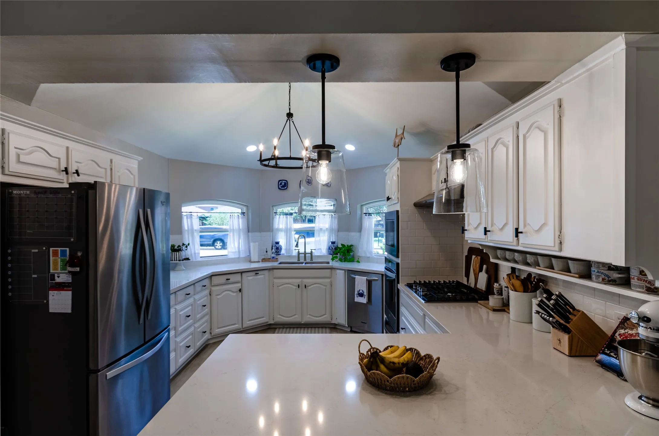 Kitchen featuring white cabinetry, light countertops, a stainless steel refrigerator, a gas cooktop, and pendant lighting